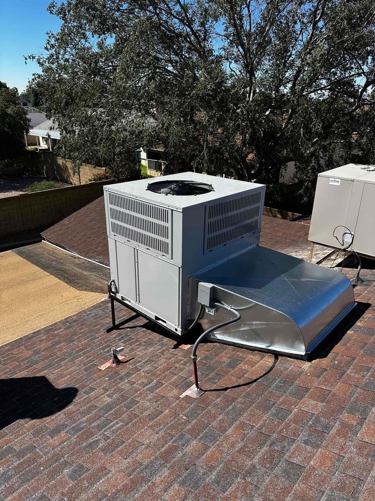 Rooftop package unit set on a raised stand with new curb adapter, sealed roof penetrations, and electrical disconnect installed.