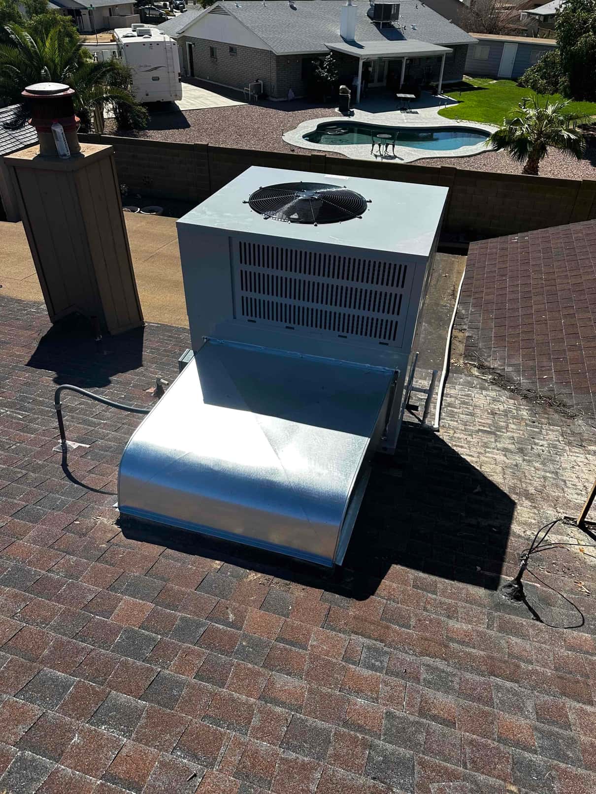 Rooftop packaged HVAC unit installed on shingle roof with new curb and duct transition, sealed and connected to electrical conduit.