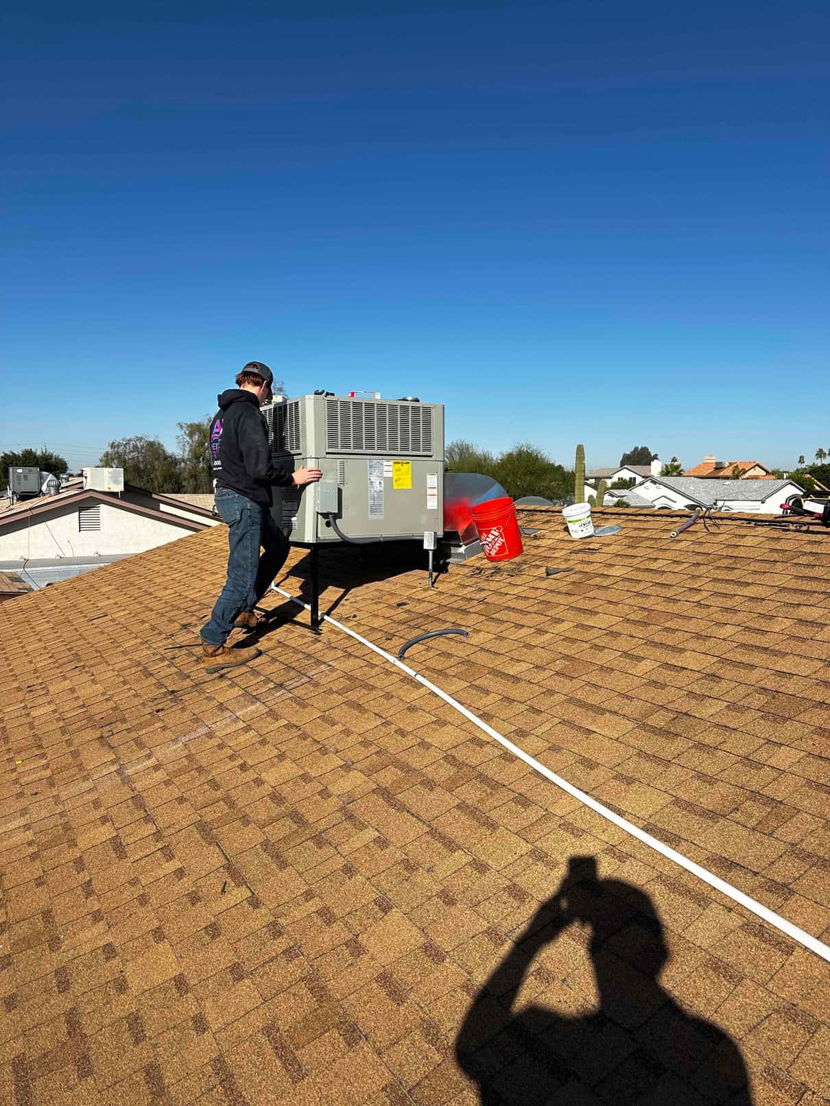 Technician works on a rooftop packaged HVAC unit set on stands, with tools and materials staged nearby on the shingles.