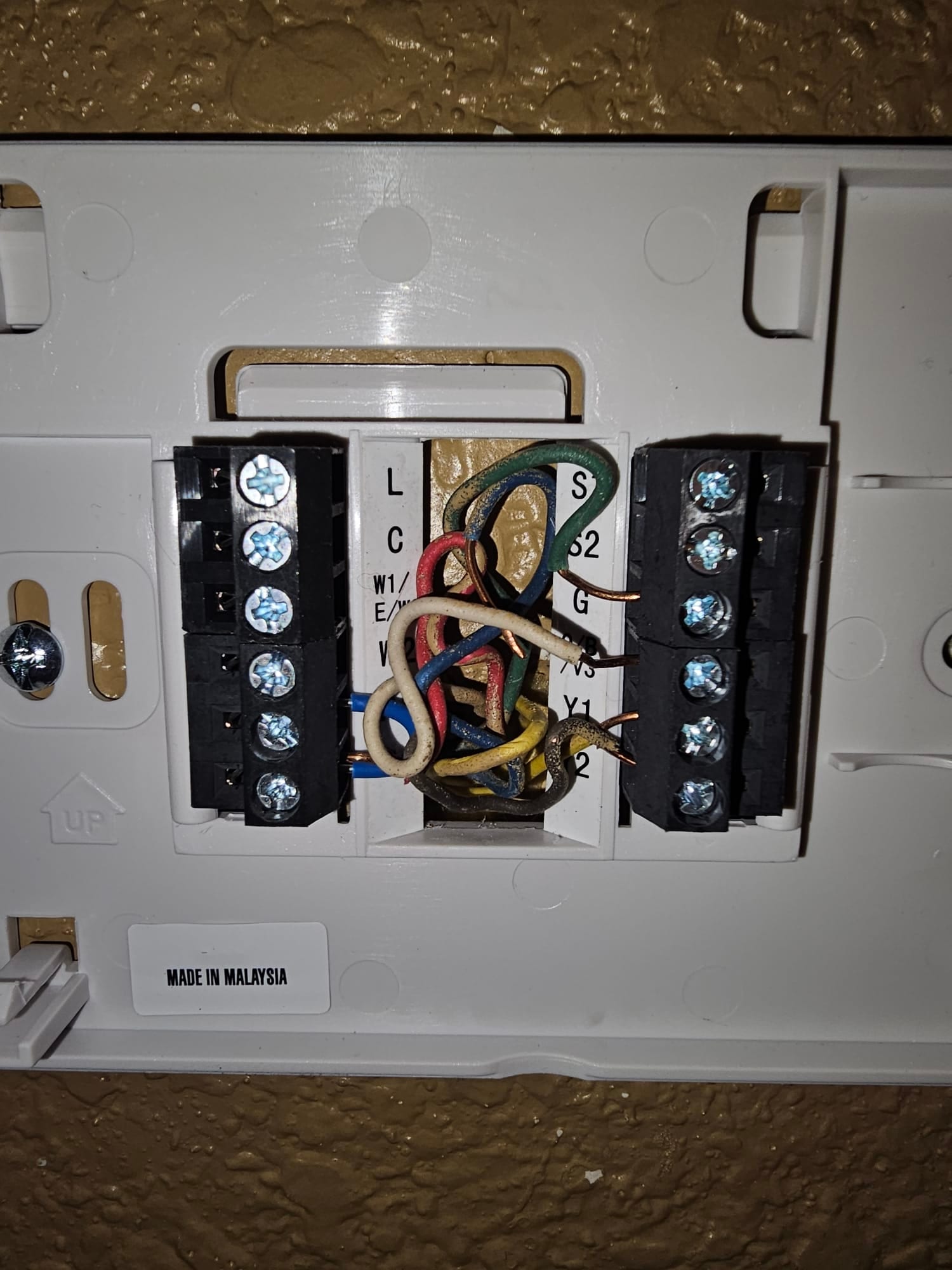 Thermostat wall plate with multi-colored control wires landed on labeled terminals, including W1/E, Y1, Y2, G, and others.