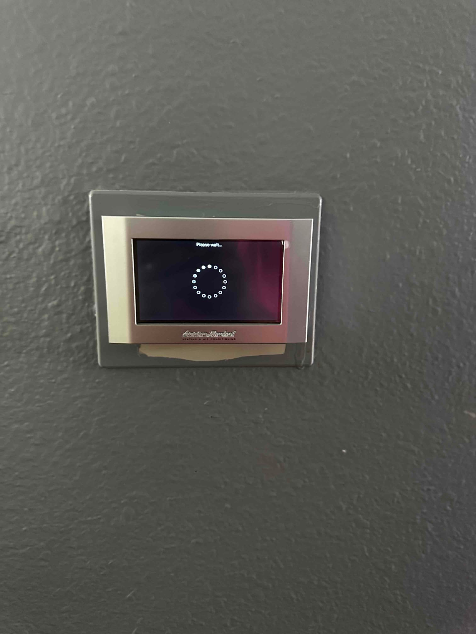 Wall-mounted digital thermostat powers up with a loading screen after installation on a newly finished HVAC system.