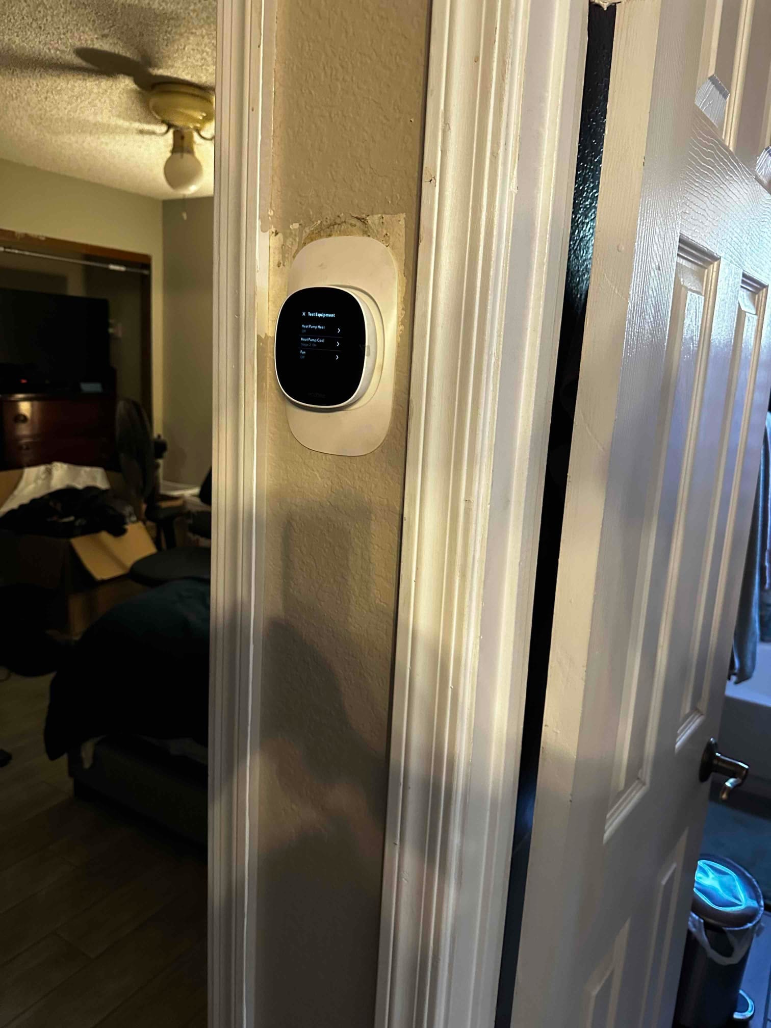 Wall-mounted smart thermostat installed on a trim plate, displaying equipment test menu during HVAC setup.