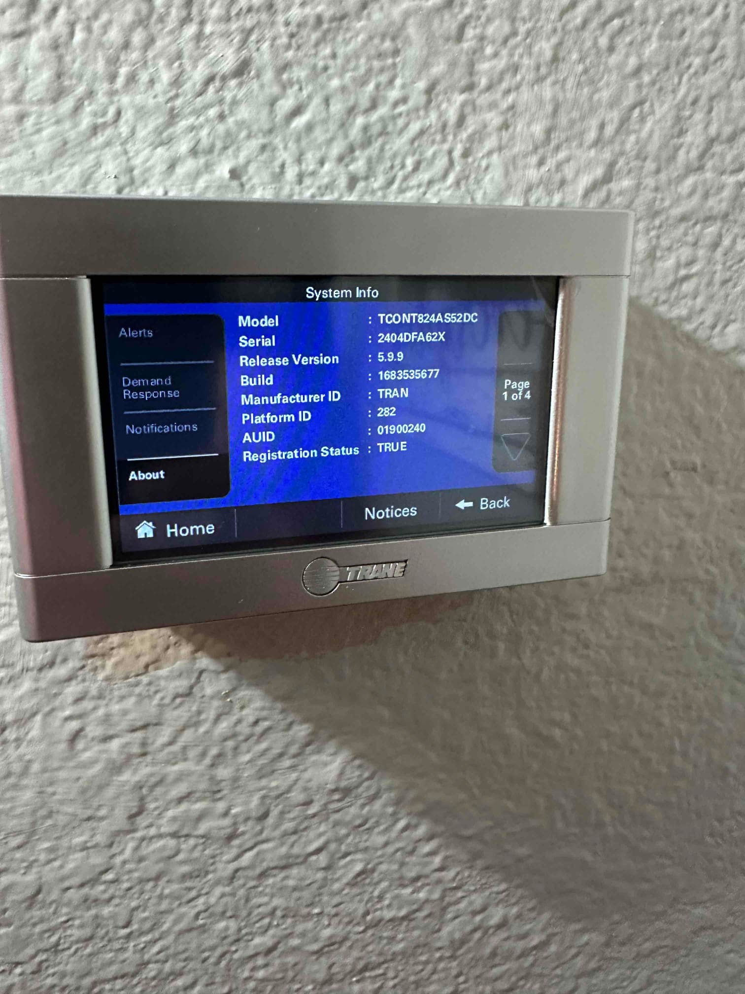 Wall-mounted touchscreen thermostat displays system information menu after installation, showing firmware and registration status on the screen.