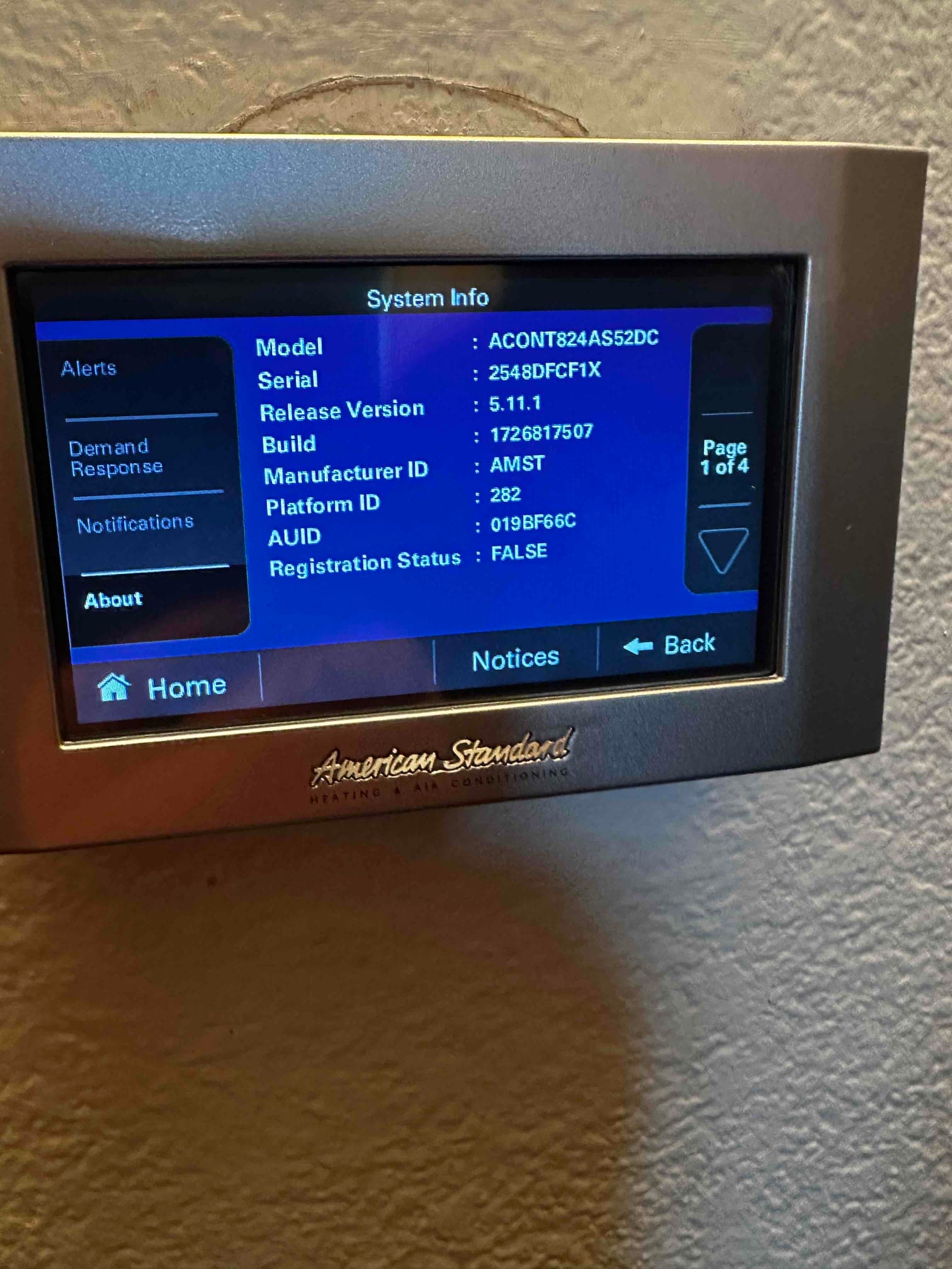 Wall-mounted touchscreen thermostat displays system information menu after installation, showing model, serial, software version, and registration status.