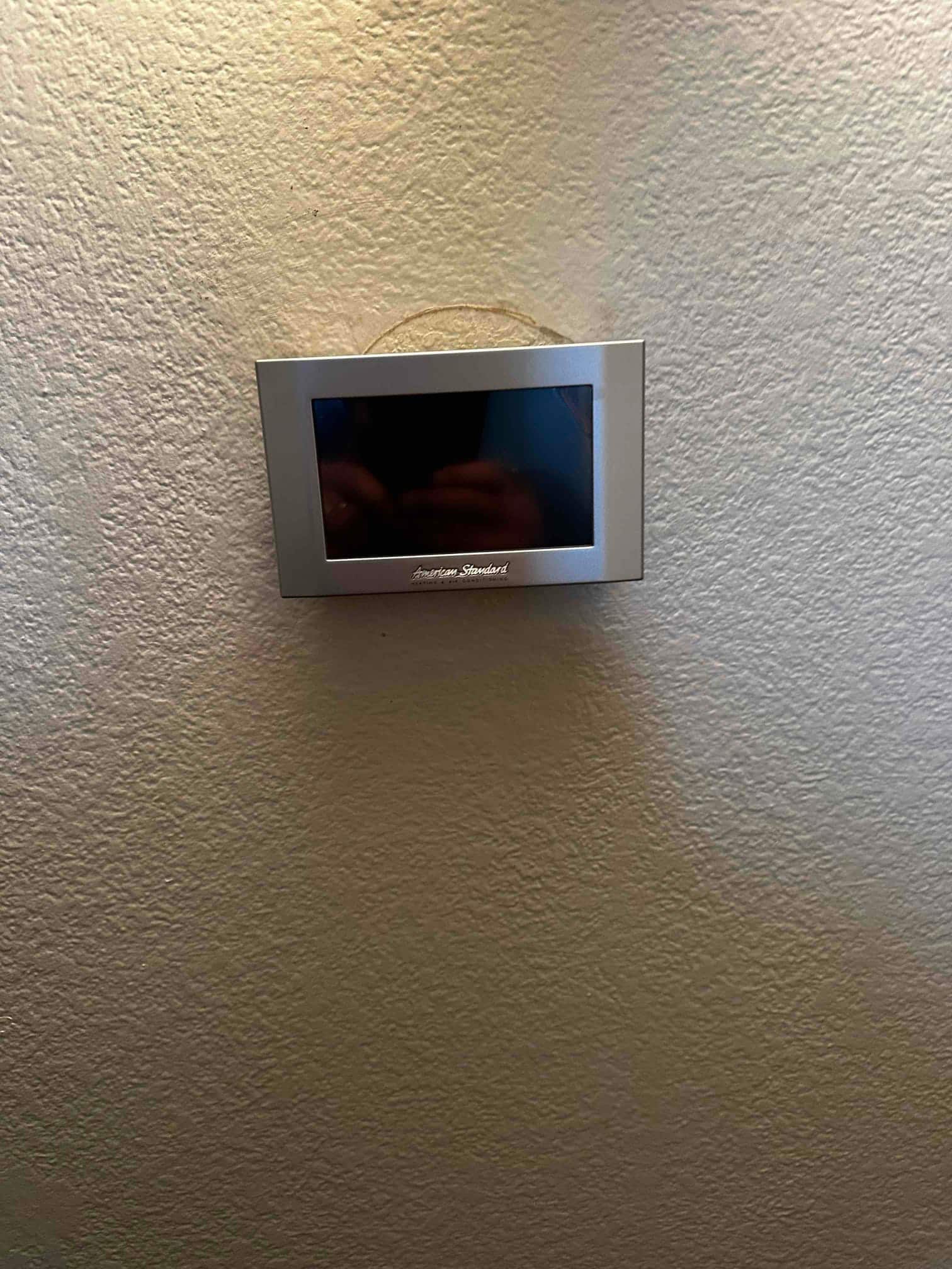 Wall-mounted touchscreen thermostat installed level on a textured interior wall, screen currently off.