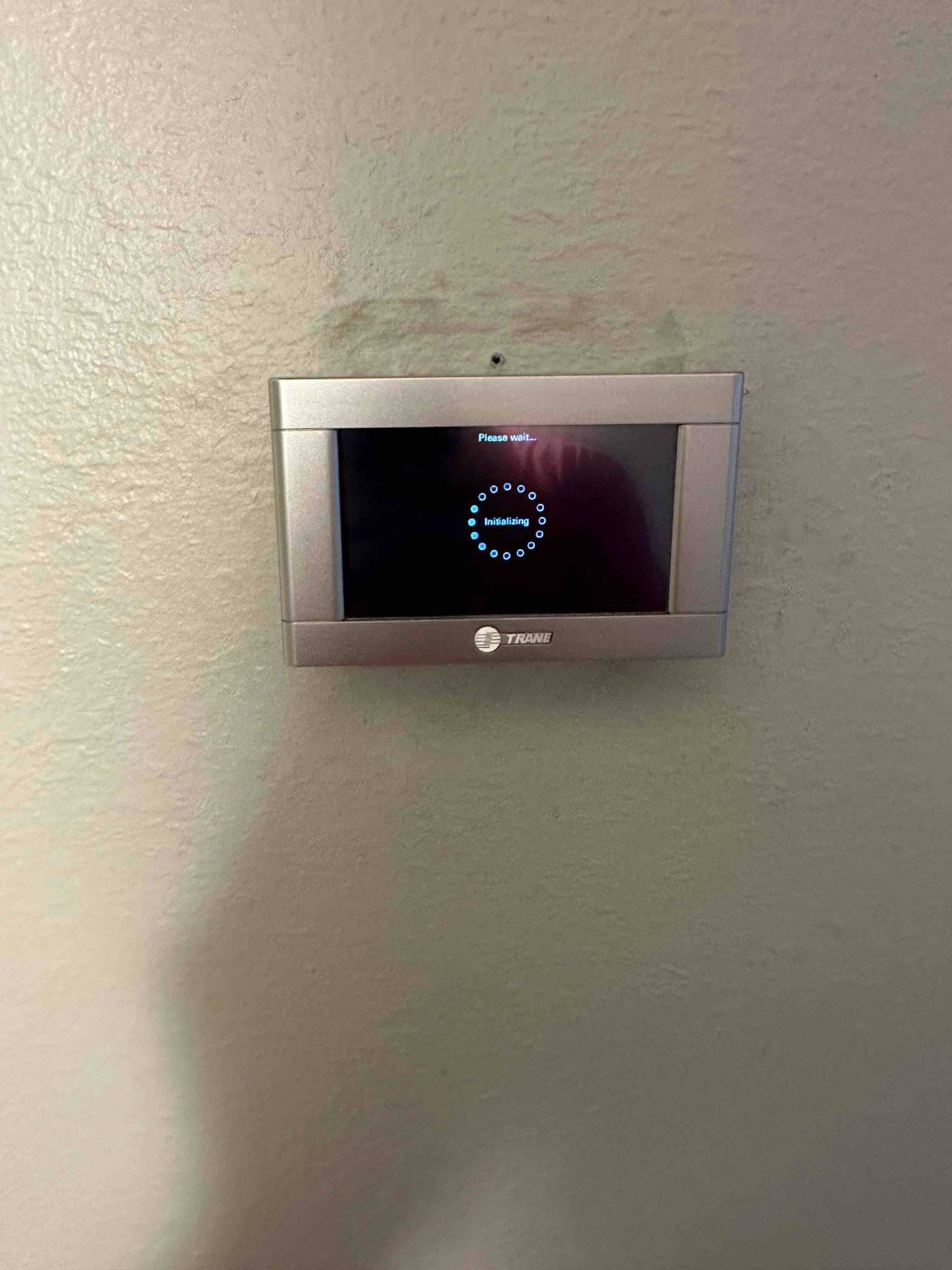 Wall-mounted touchscreen thermostat powers on with an initializing message during commissioning after HVAC installation.
