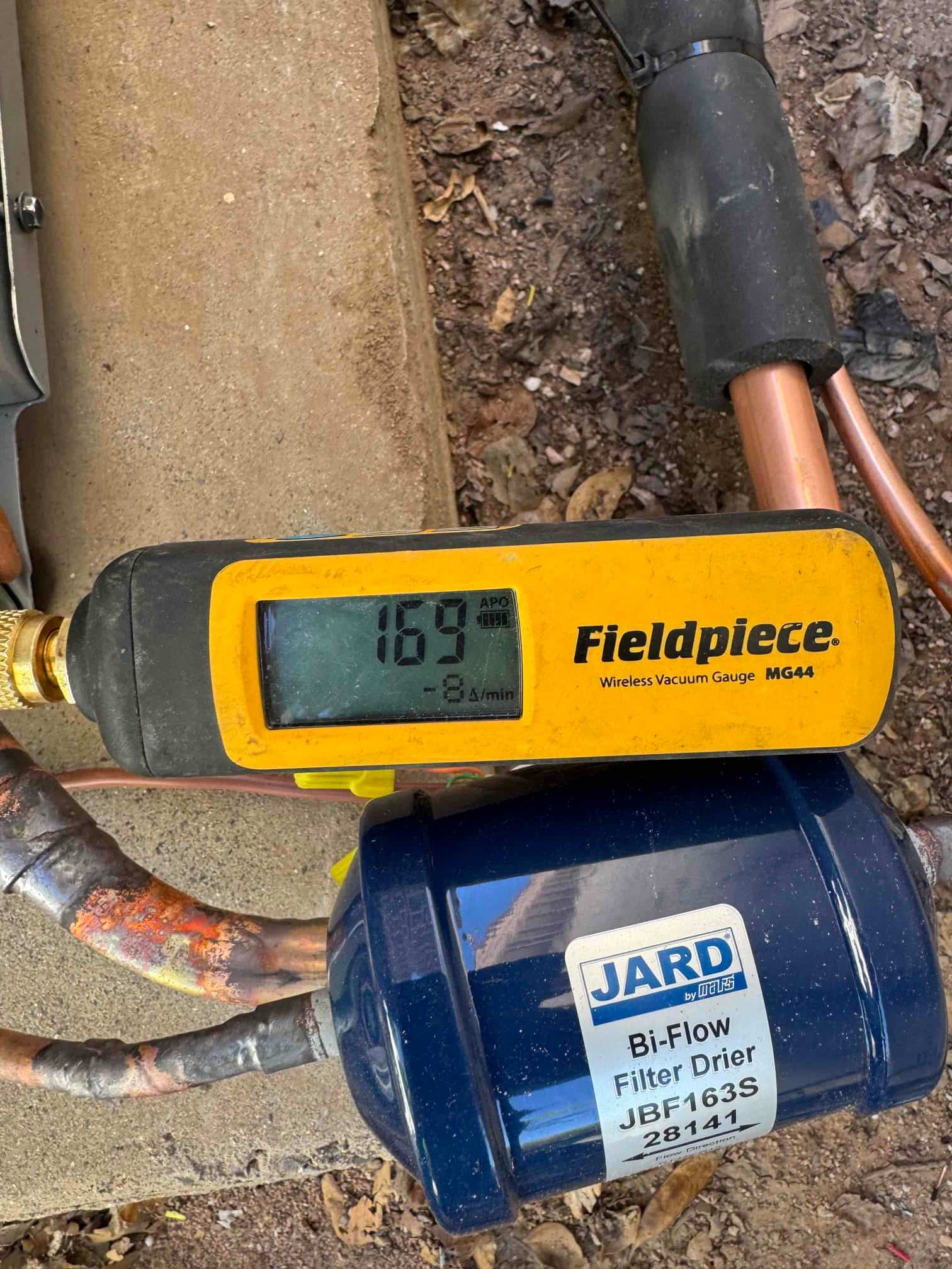 Wireless vacuum gauge shows 169 microns while evacuating the system near a bi-flow filter drier and copper tubing.