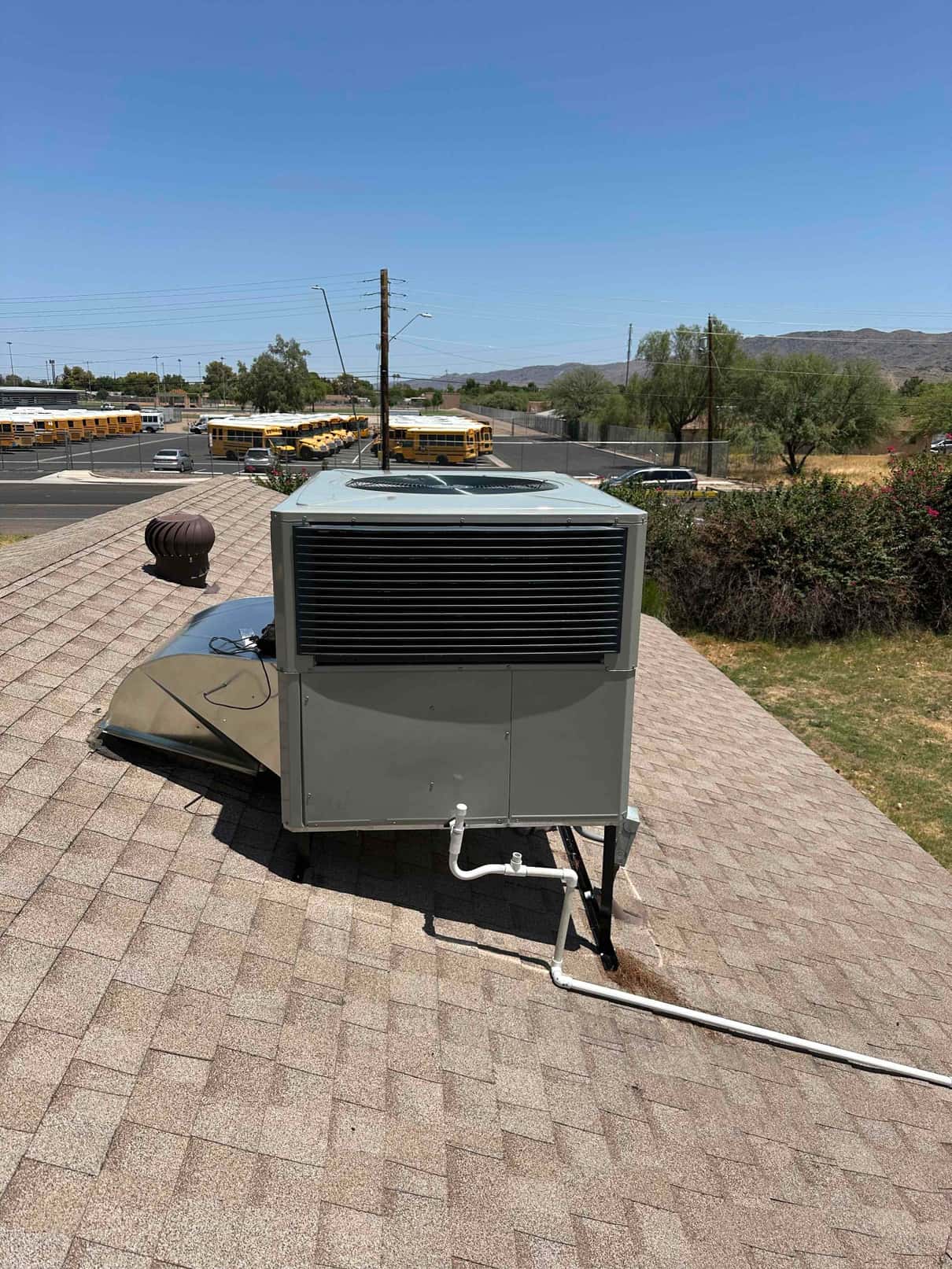 New rooftop packaged heat pump installed on shingles with sealed curb, condensate drain piping routed across the roof, and secure support legs.