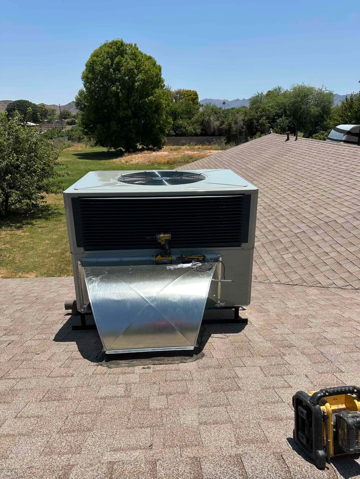 Rooftop packaged HVAC unit newly installed with sheet metal curb and sealed roof penetration visible on the shingle roof.
