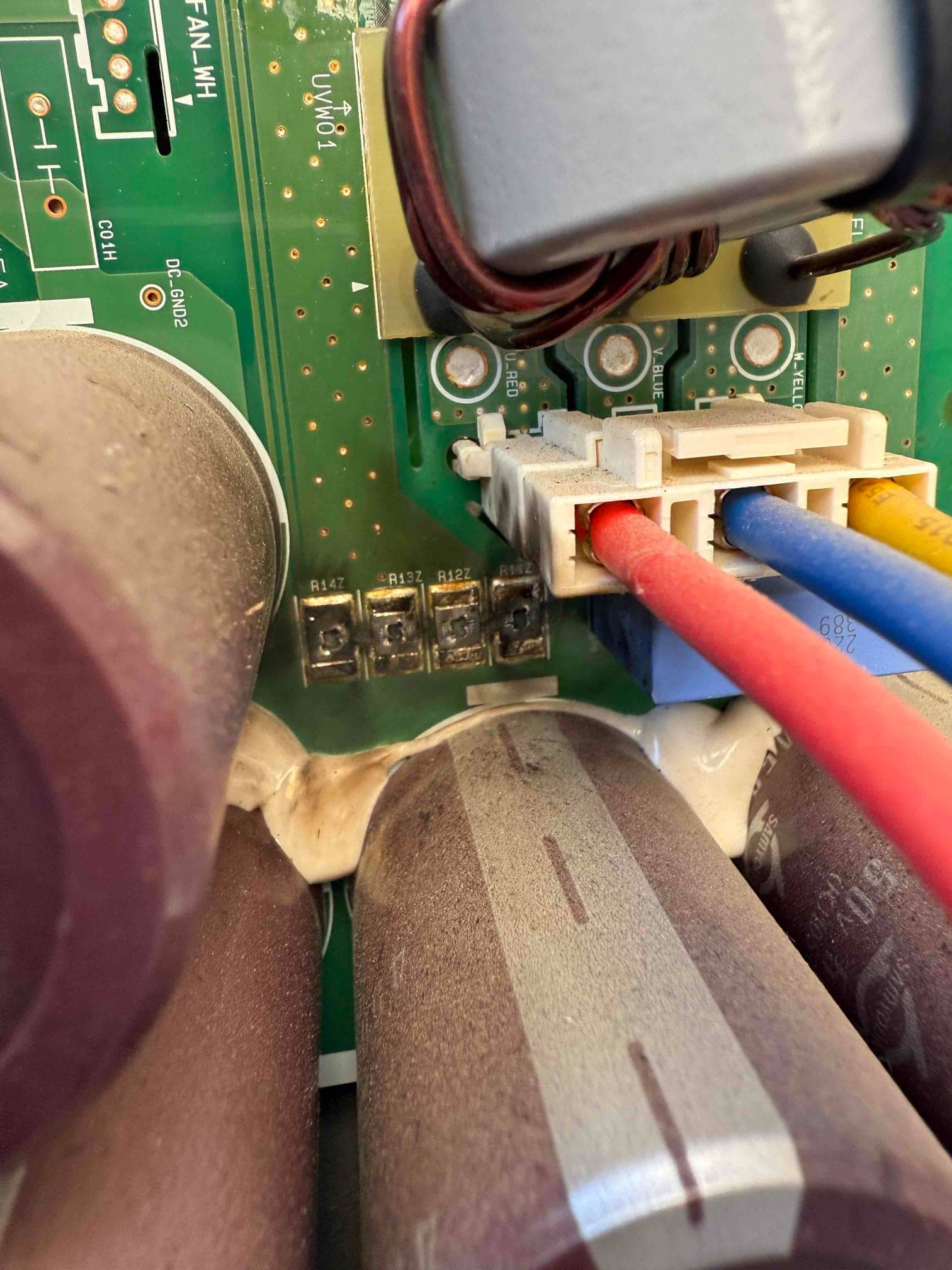 Close-up of an outdoor inverter control board showing large capacitors, resistors labeled R347–R357, and a multi-wire connector with heat discoloration.