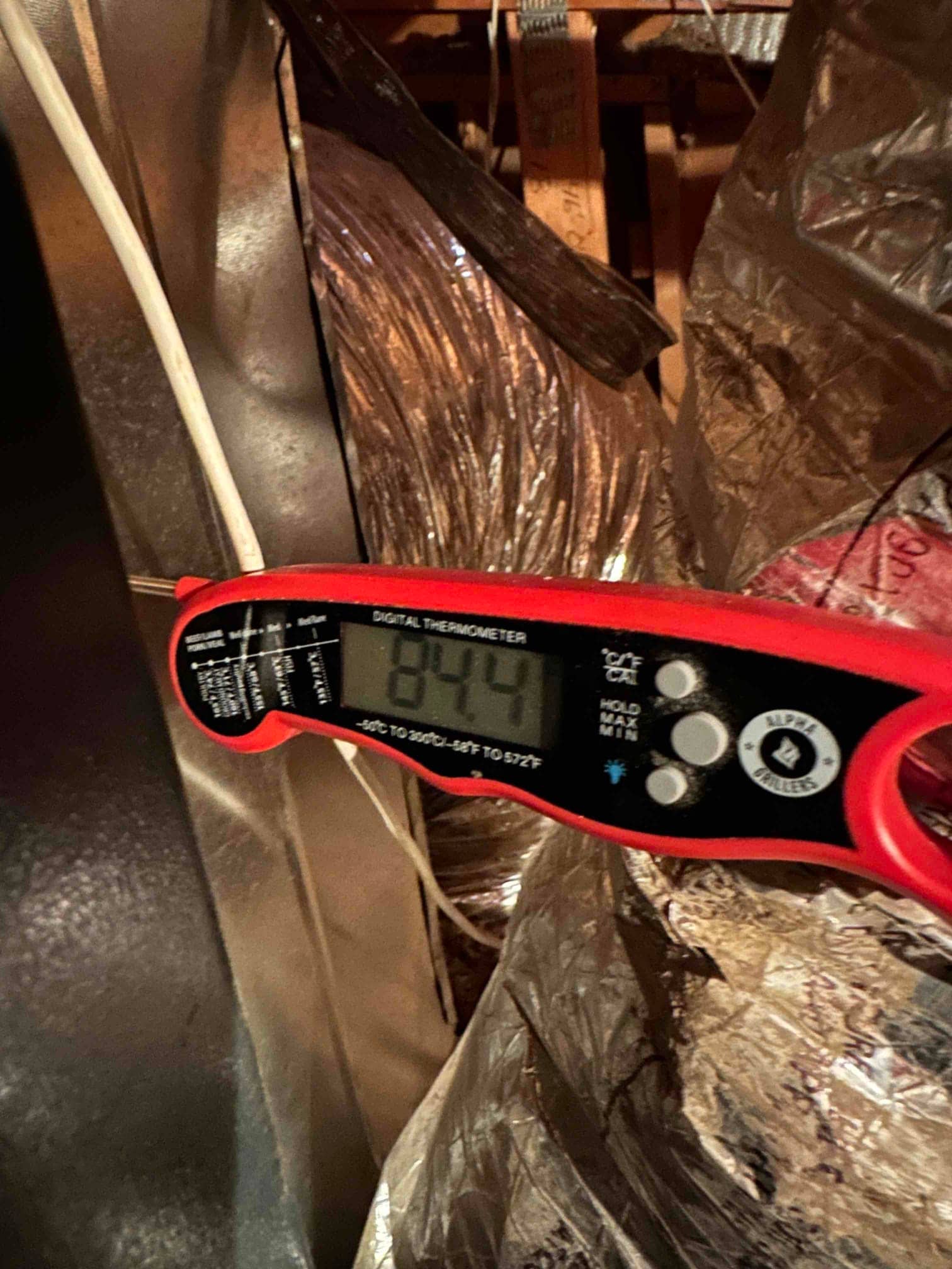Digital thermometer probe measures return air temperature at 84°F near insulated ducting during system commissioning.