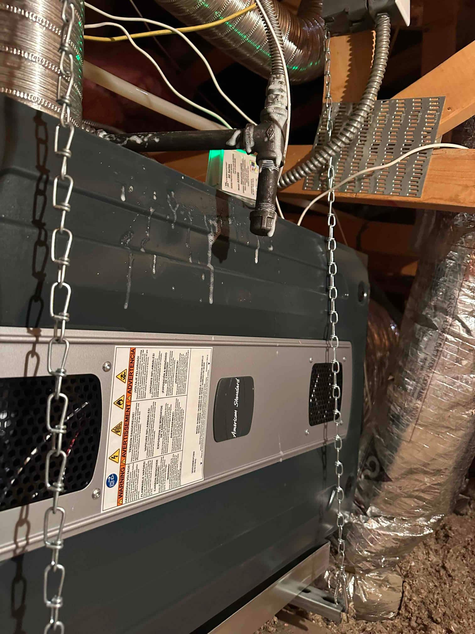 Horizontal air handler suspended from joists with chains, connected to flex duct and electrical whip, with condensate piping and trap visible.