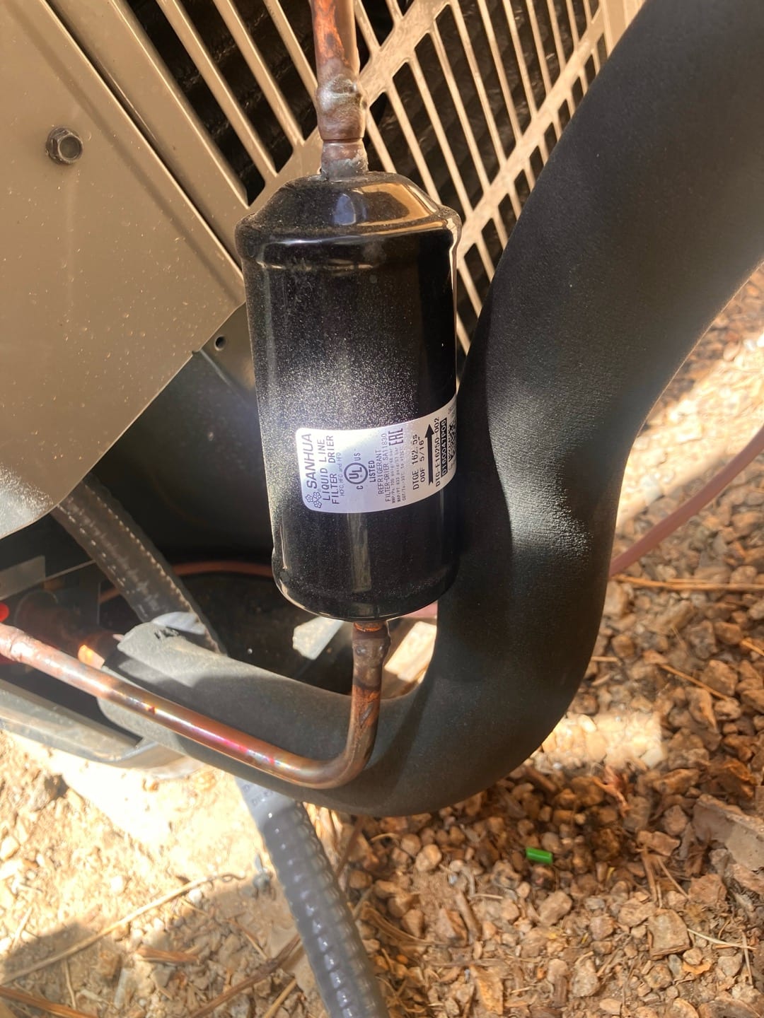Liquid-line filter drier brazed into the refrigerant circuit beside the outdoor condenser, with insulated suction line routed nearby.
