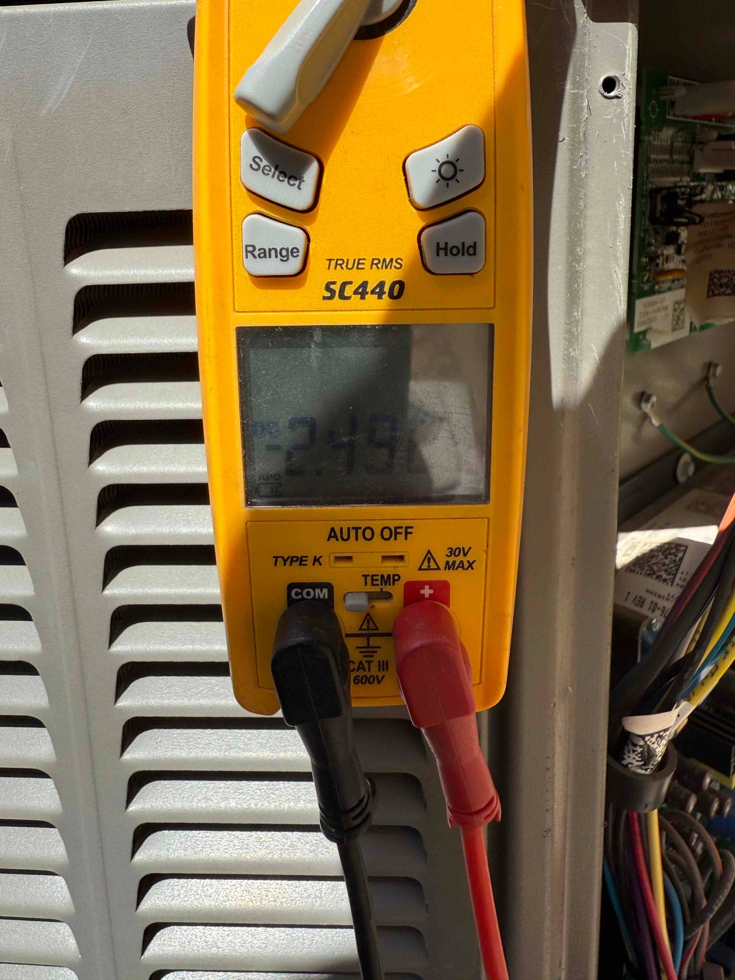 Multimeter measures 23.197 V across two leads at the outdoor unit control wiring during repair.