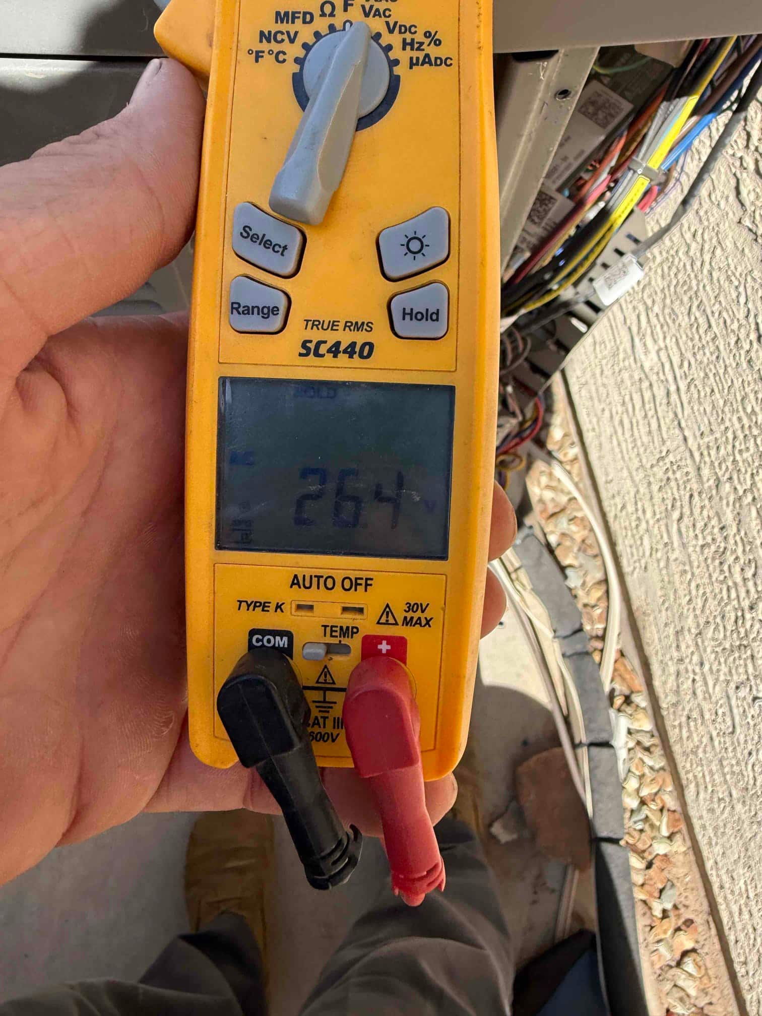 Multimeter measures 26.47 V at the outdoor unit wiring during diagnostic testing.