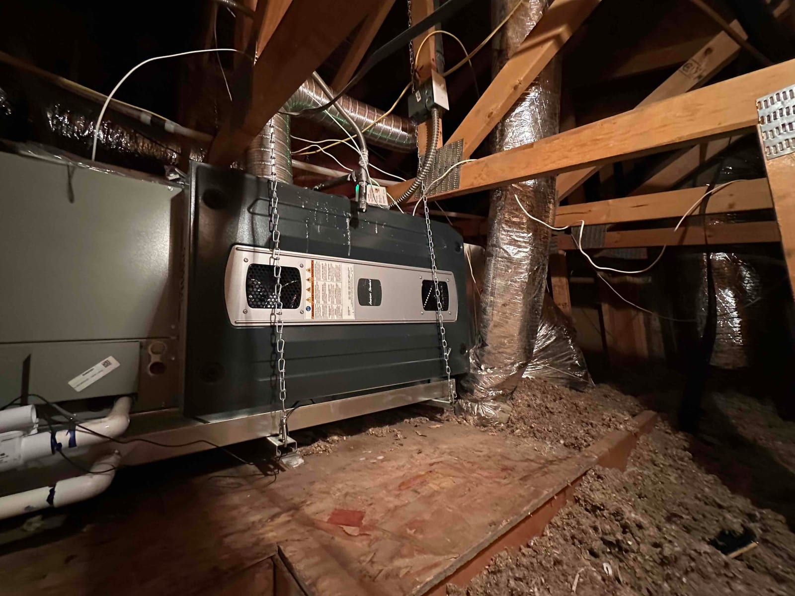 New attic air handler suspended with chains, connected to insulated ductwork and condensate drain, with electrical whip and support platform.