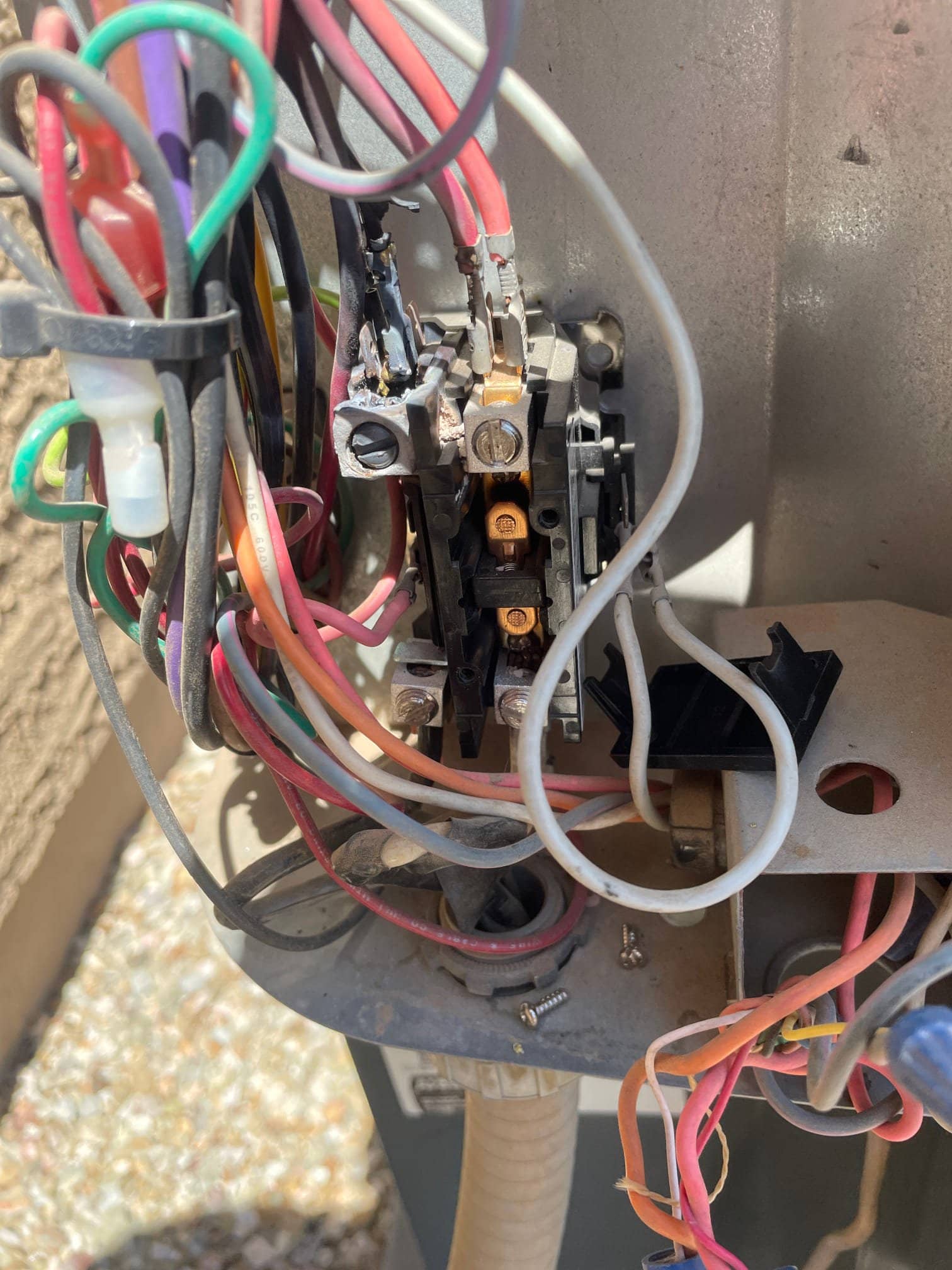 Outdoor condenser contactor with multiple connected wires, showing dark discoloration and melted insulation at a left terminal.