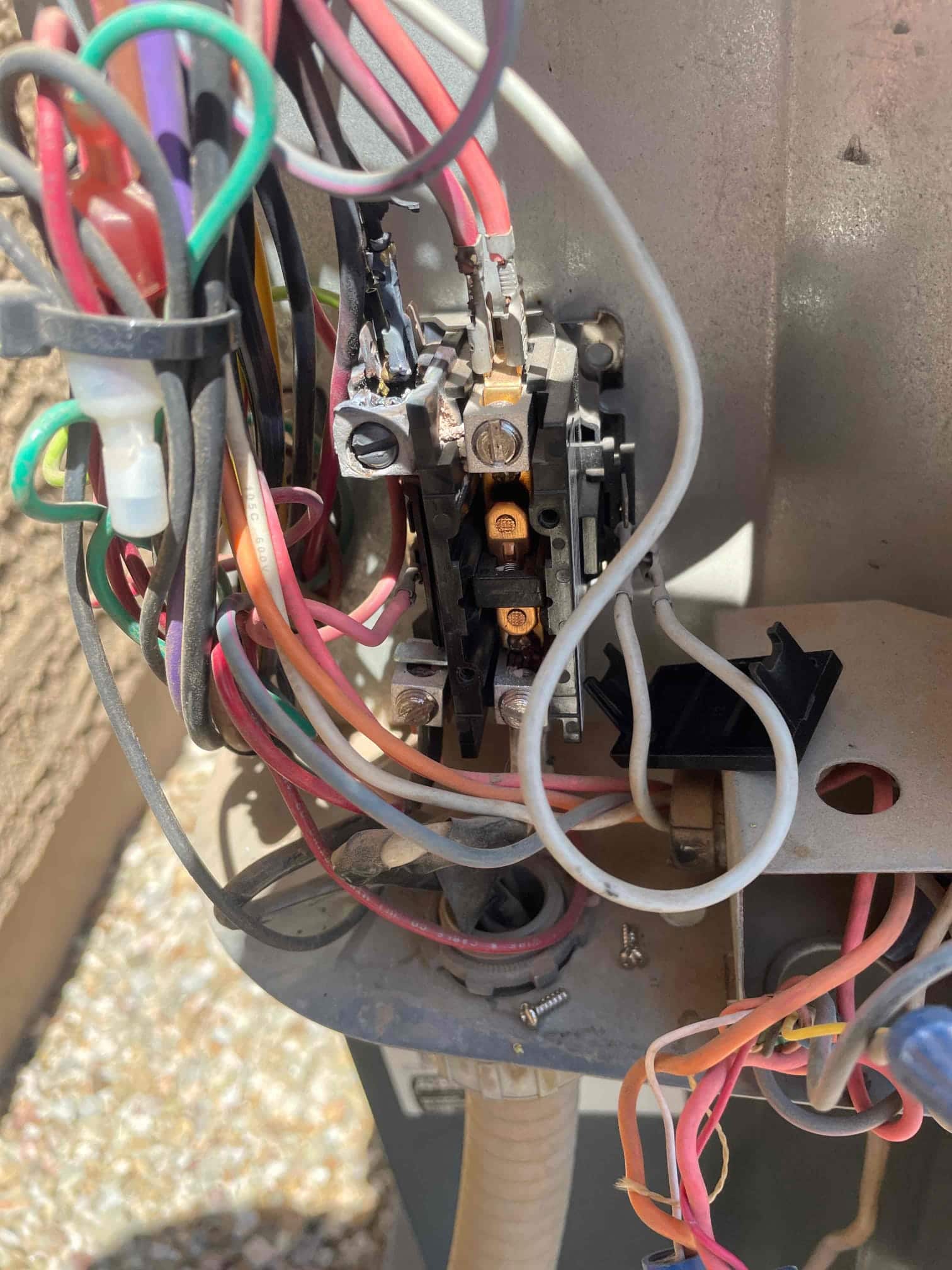 Outdoor condenser contactor with multiple wires connected; left terminal shows heavy charring and heat damage.