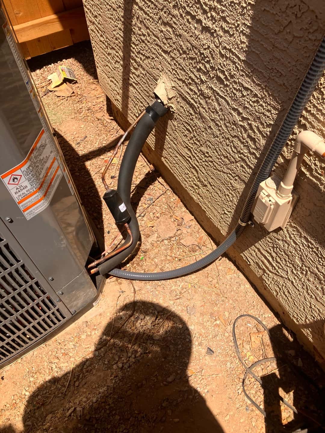 Outdoor condenser set with insulated suction line, liquid line, sealed wall penetration, and electrical whip to the disconnect.