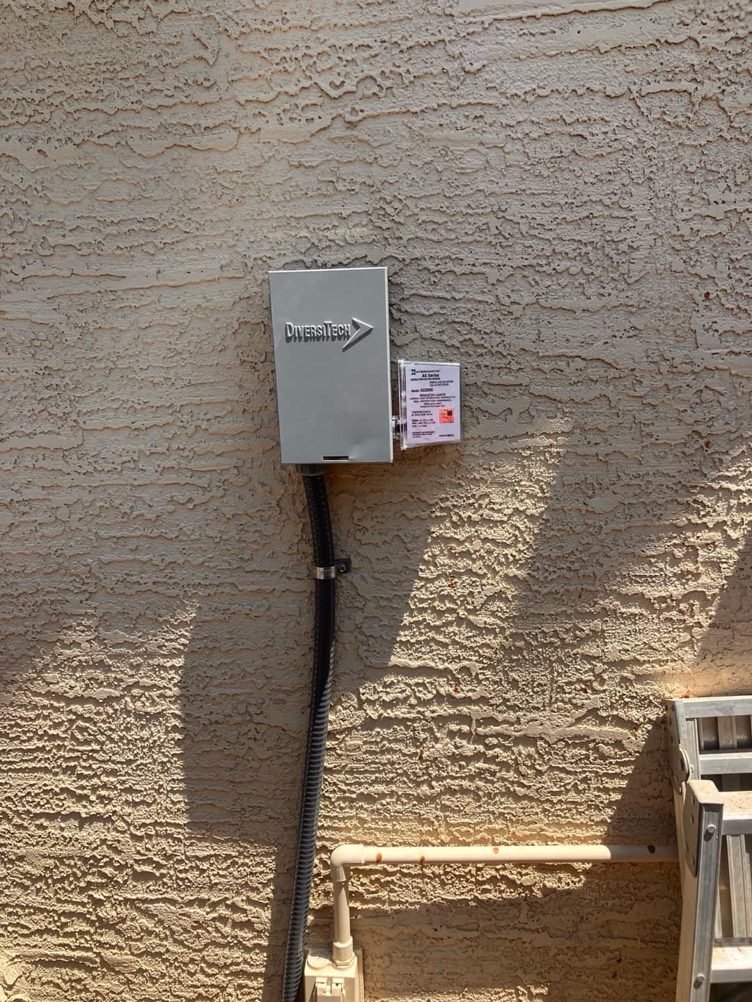 Outdoor HVAC disconnect box mounted on stucco wall with flexible conduit routed down to the service entry.