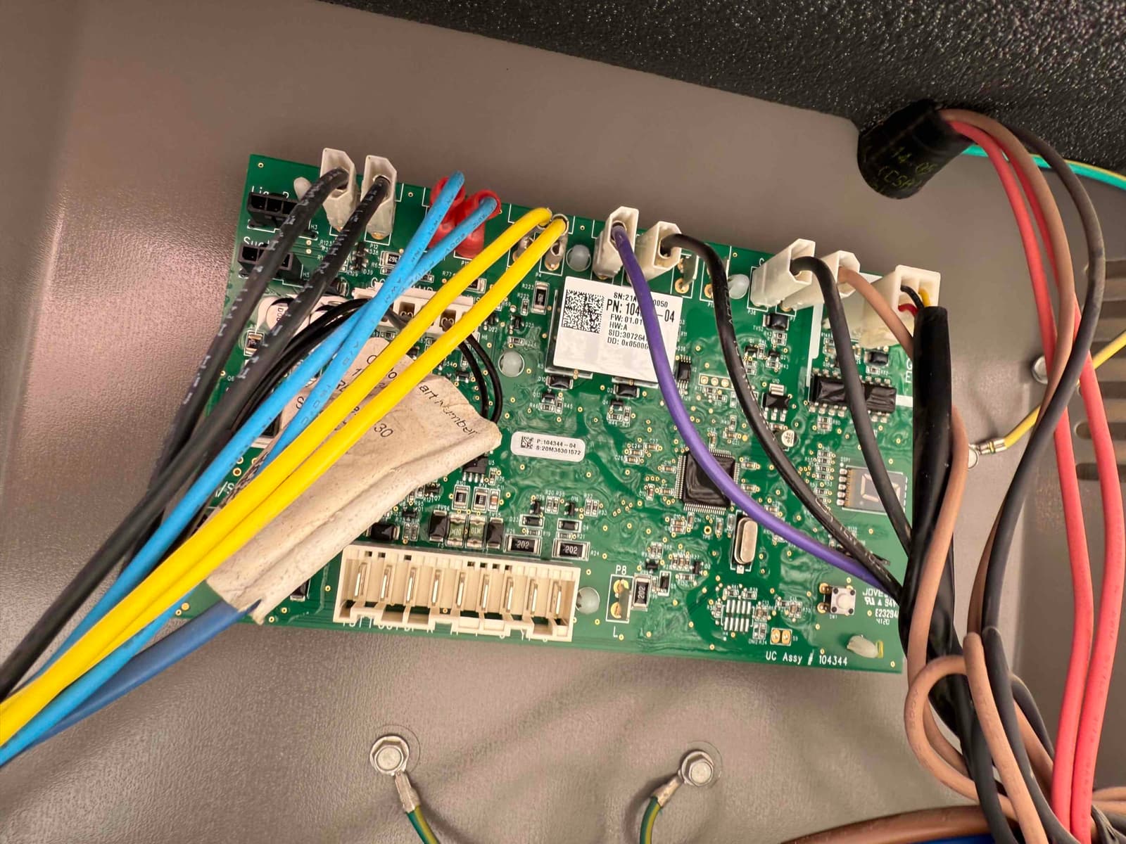 Outdoor unit control board with multiple color-coded wires connected to screw terminals and plug-in connectors inside the condenser cabinet.