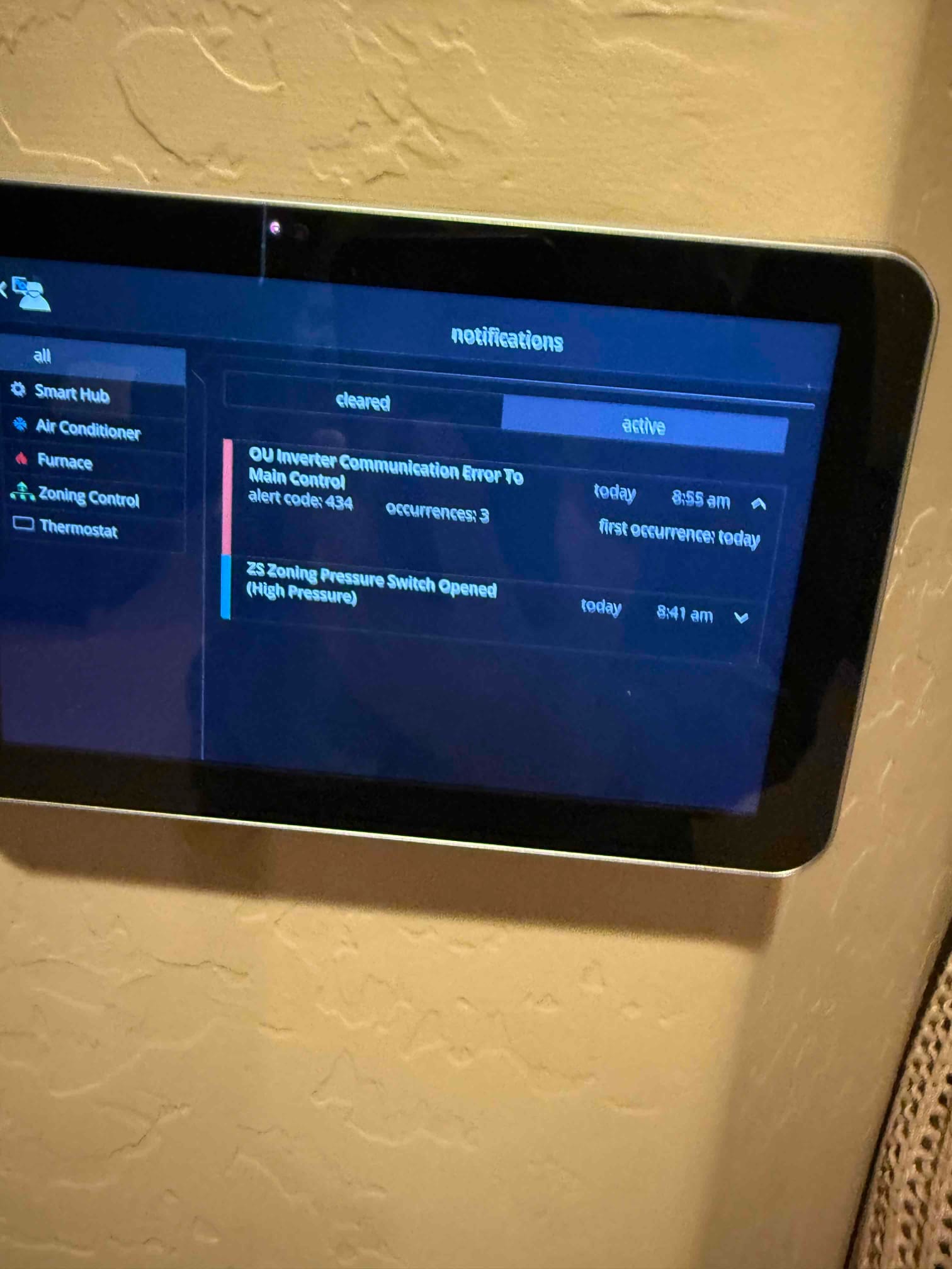 Wall-mounted HVAC control screen shows active notifications for inverter communication error and zone pressure switch opened.