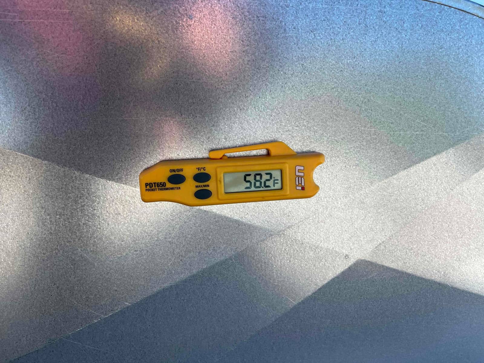 Digital thermometer shows 58.2°F while measuring air during HVAC commissioning on a metal duct surface.