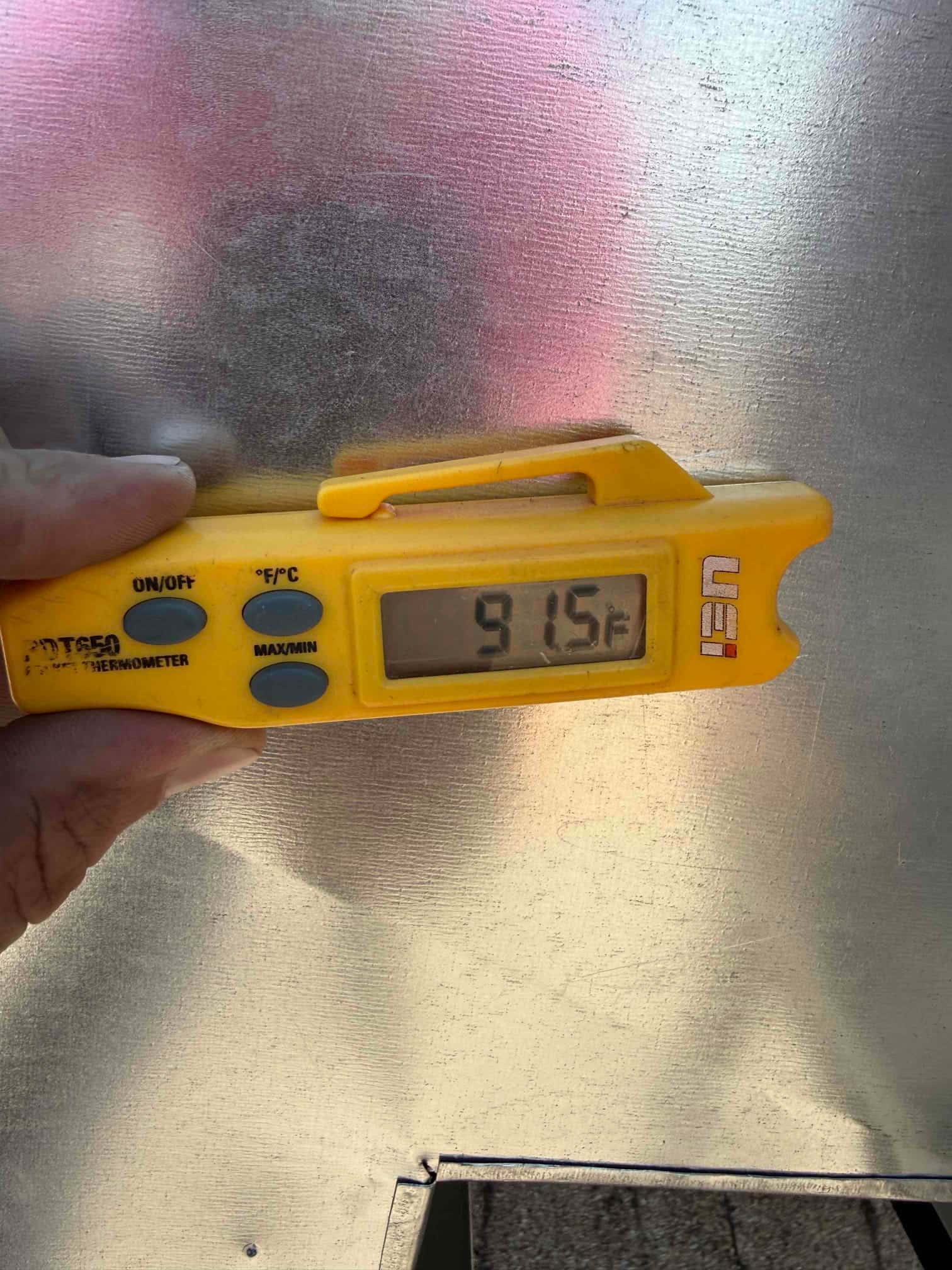 Digital thermometer shows 91.5°F while checking air temperature at the HVAC installation site.