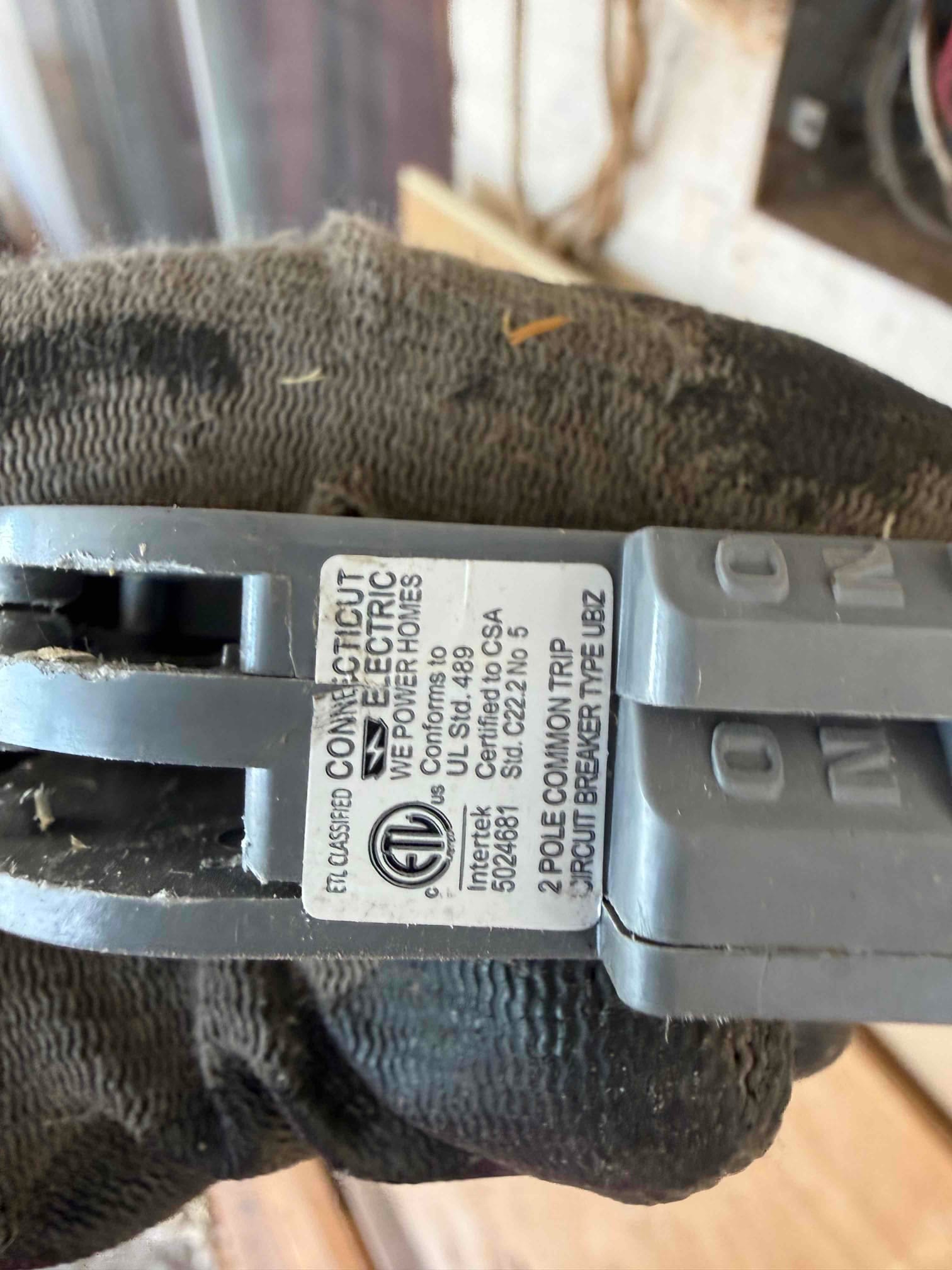 Gloved hand holds a two-pole circuit breaker labeled common trip, part of the HVAC electrical disconnect or panel work.