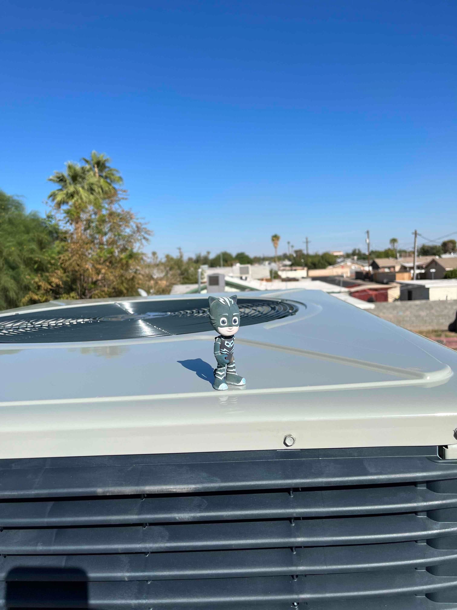 New outdoor condenser installed on roof, showing fan guard and cabinet with clean horizontal louvers under clear sky.