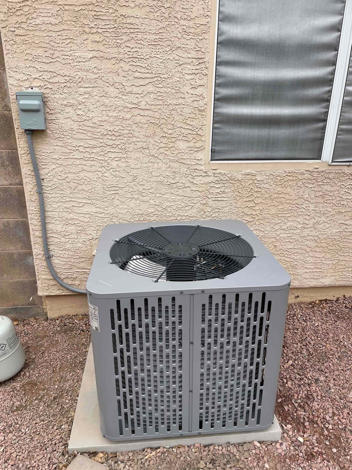 New outdoor condenser set on a level pad beside the home with weatherproof electrical disconnect mounted on the wall.