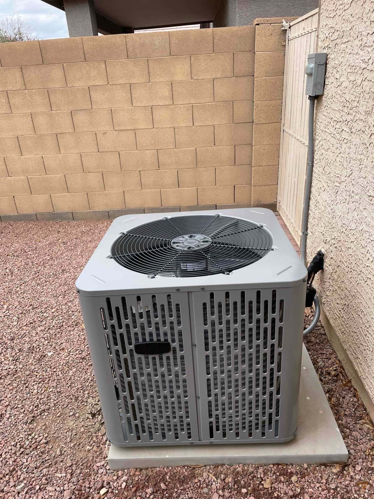 New outdoor condenser set on a level pad with insulated line set and weatherproof disconnect mounted on the wall.
