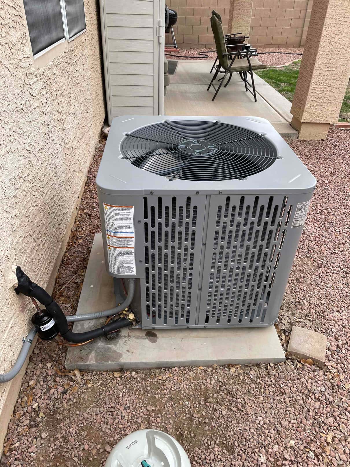 New outdoor condenser set on a level pad with insulated refrigerant lines, service valves capped, and electrical whip connected.