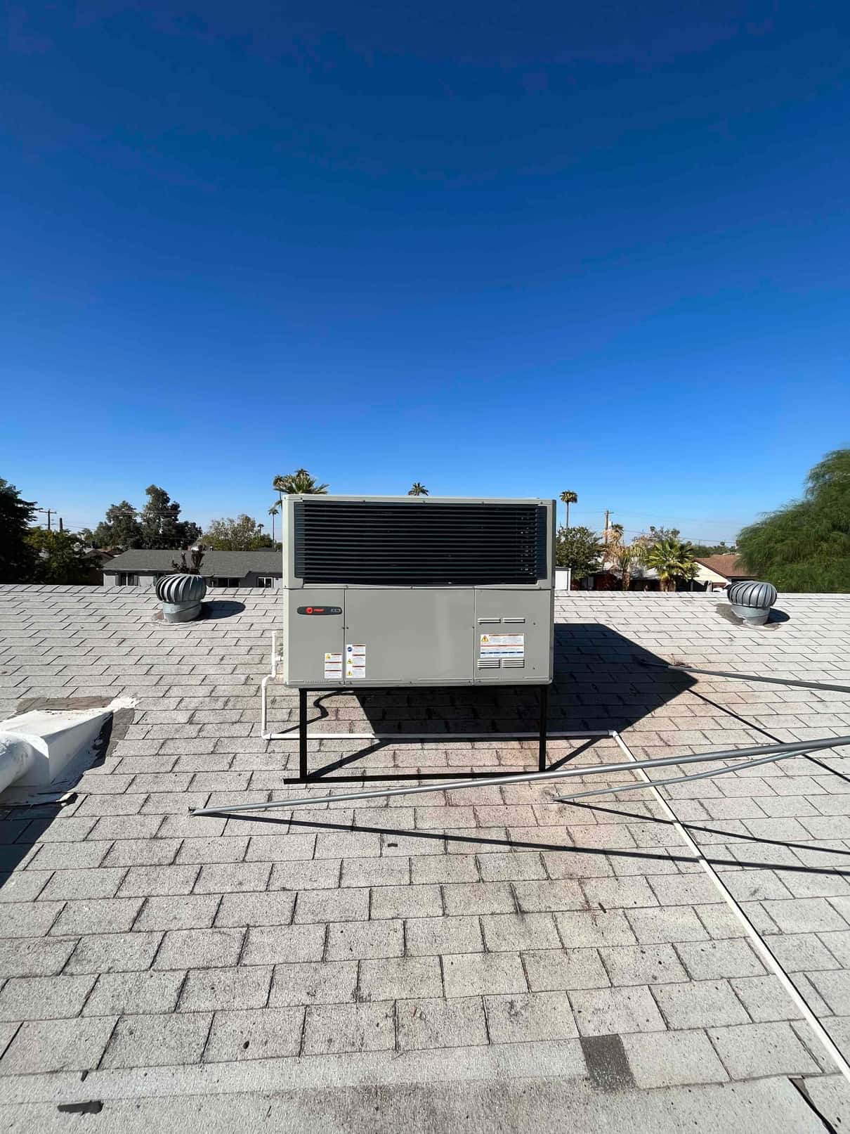 New rooftop packaged HVAC unit installed on a raised stand with sealed roof penetrations and visible condensate drain routing.