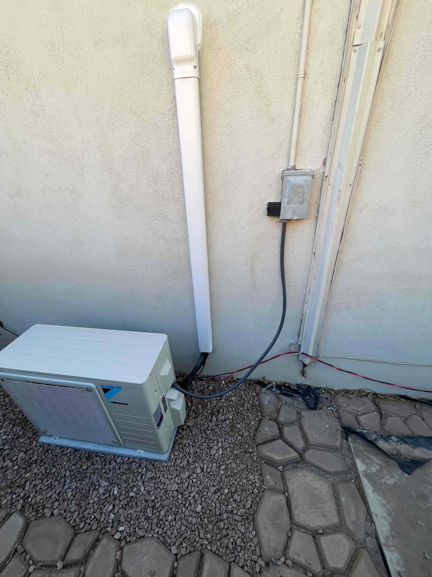 Outdoor mini-split condenser set on a level pad with line set cover and weatherproof disconnect installed on the wall.