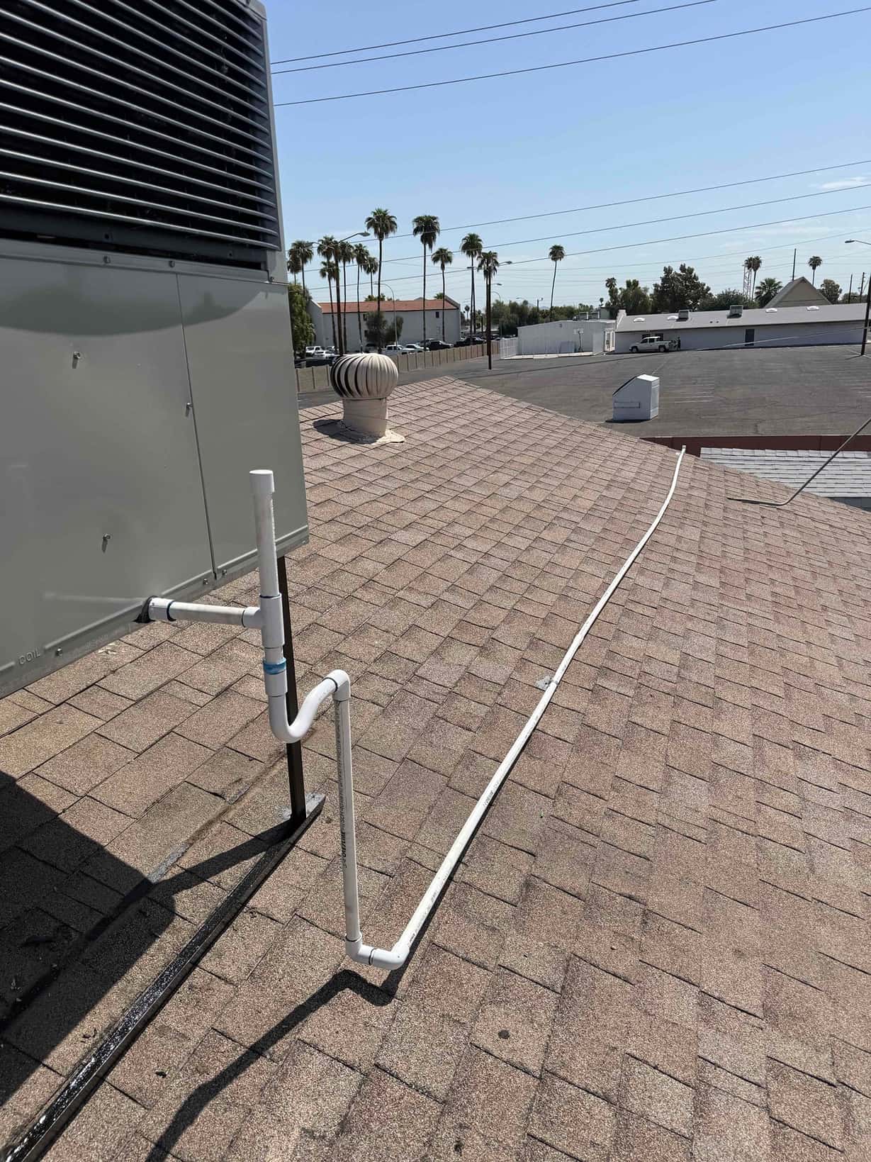 PVC condensate drain piping routed from the rooftop package unit across the shingle roof with proper trap and slope.