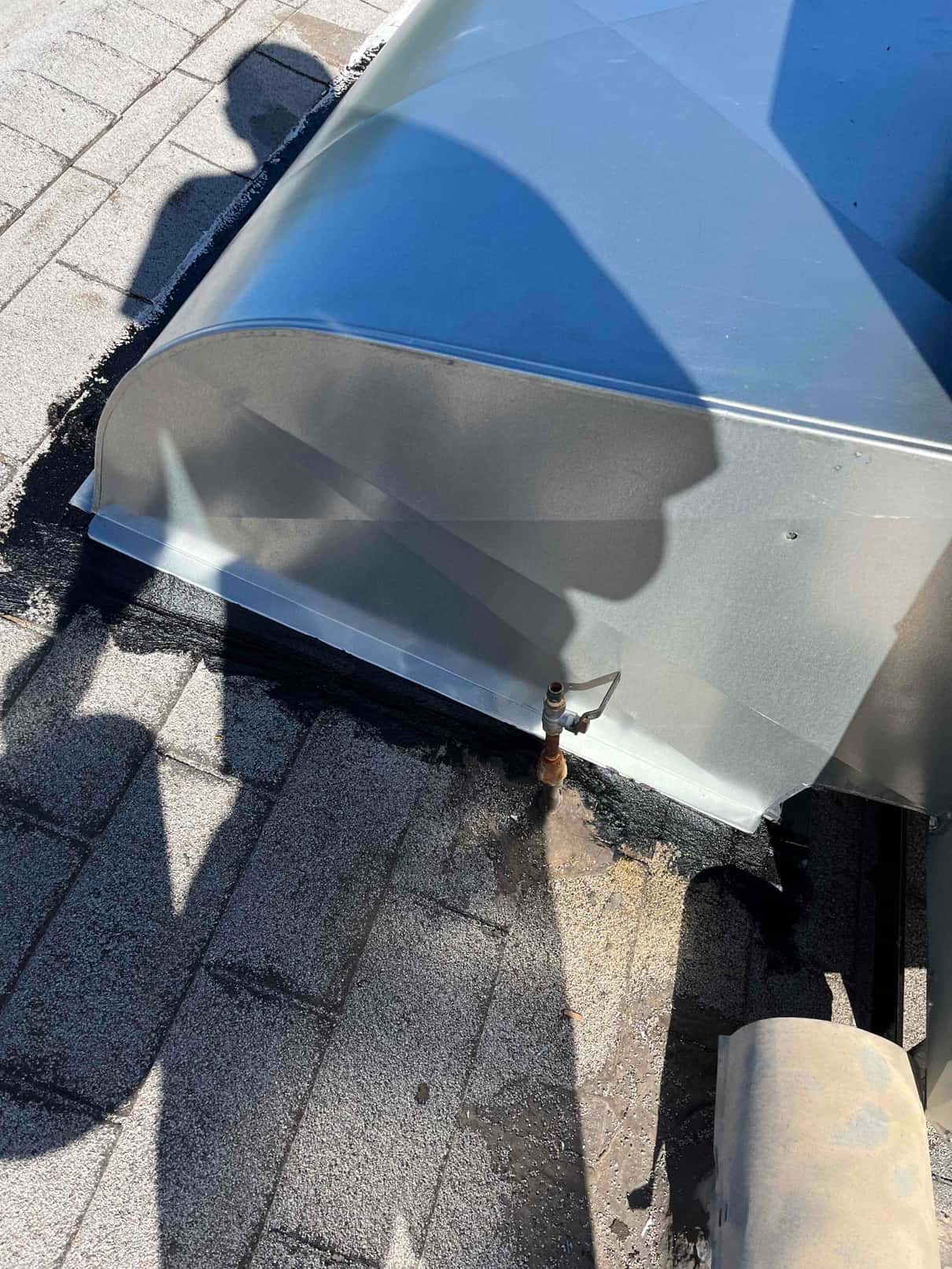 Roof curb or duct transition flashing is sealed to the roof membrane, with a nearby gas or water shutoff valve visible.