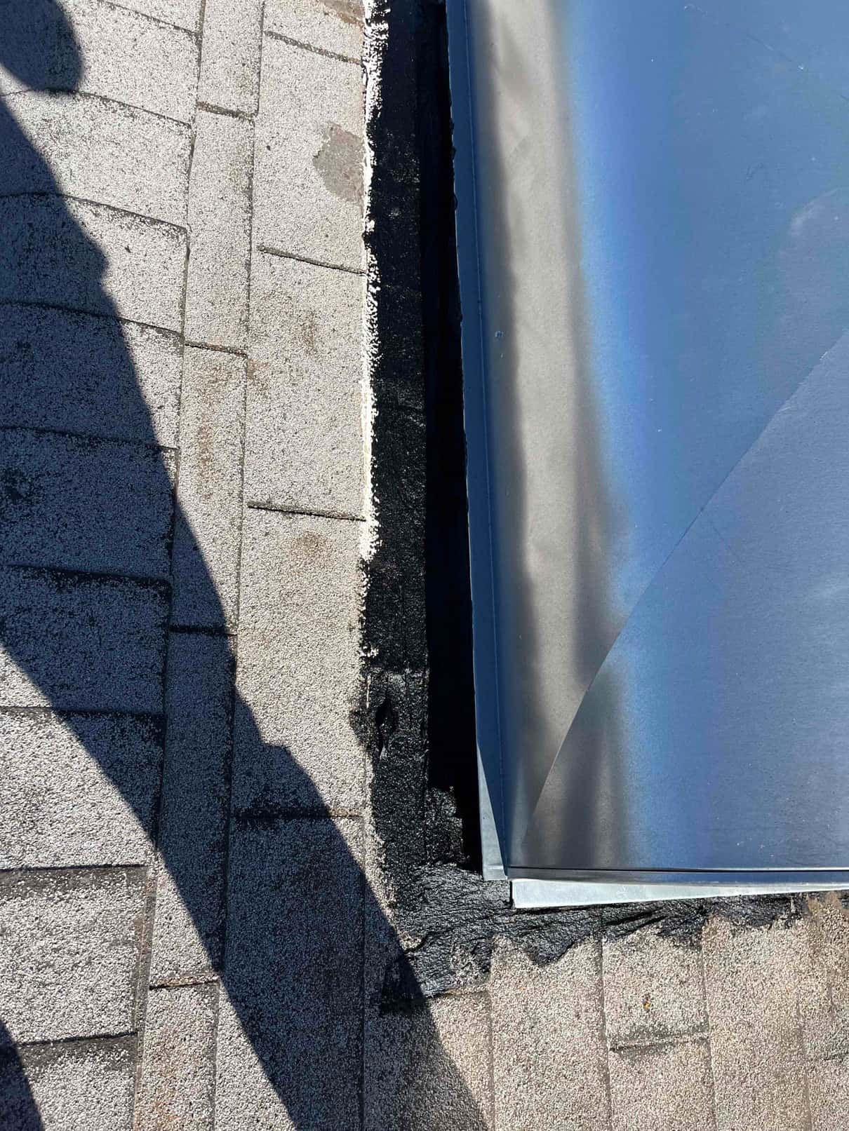 Roof curb or flashing detail sealed to roofing with black mastic around a metal duct or equipment curb.
