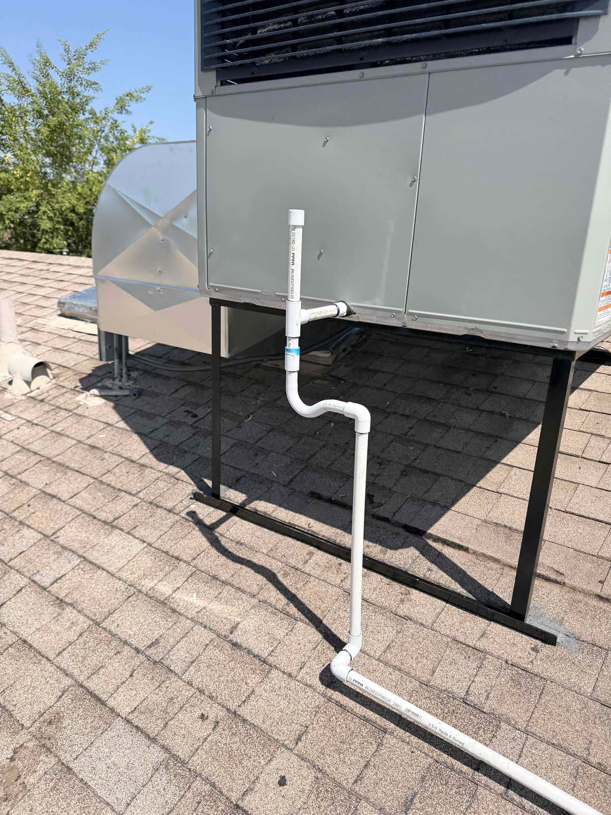 Roof-mounted package unit with newly installed PVC condensate drain piping routed across the shingles from the cabinet drain port.