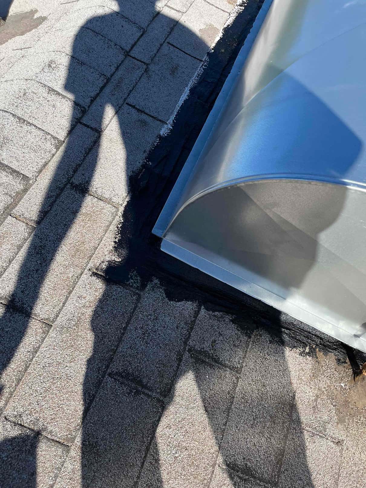Roof penetration flashing at a metal duct curb sealed with roofing mastic around shingles to ensure a watertight HVAC install.