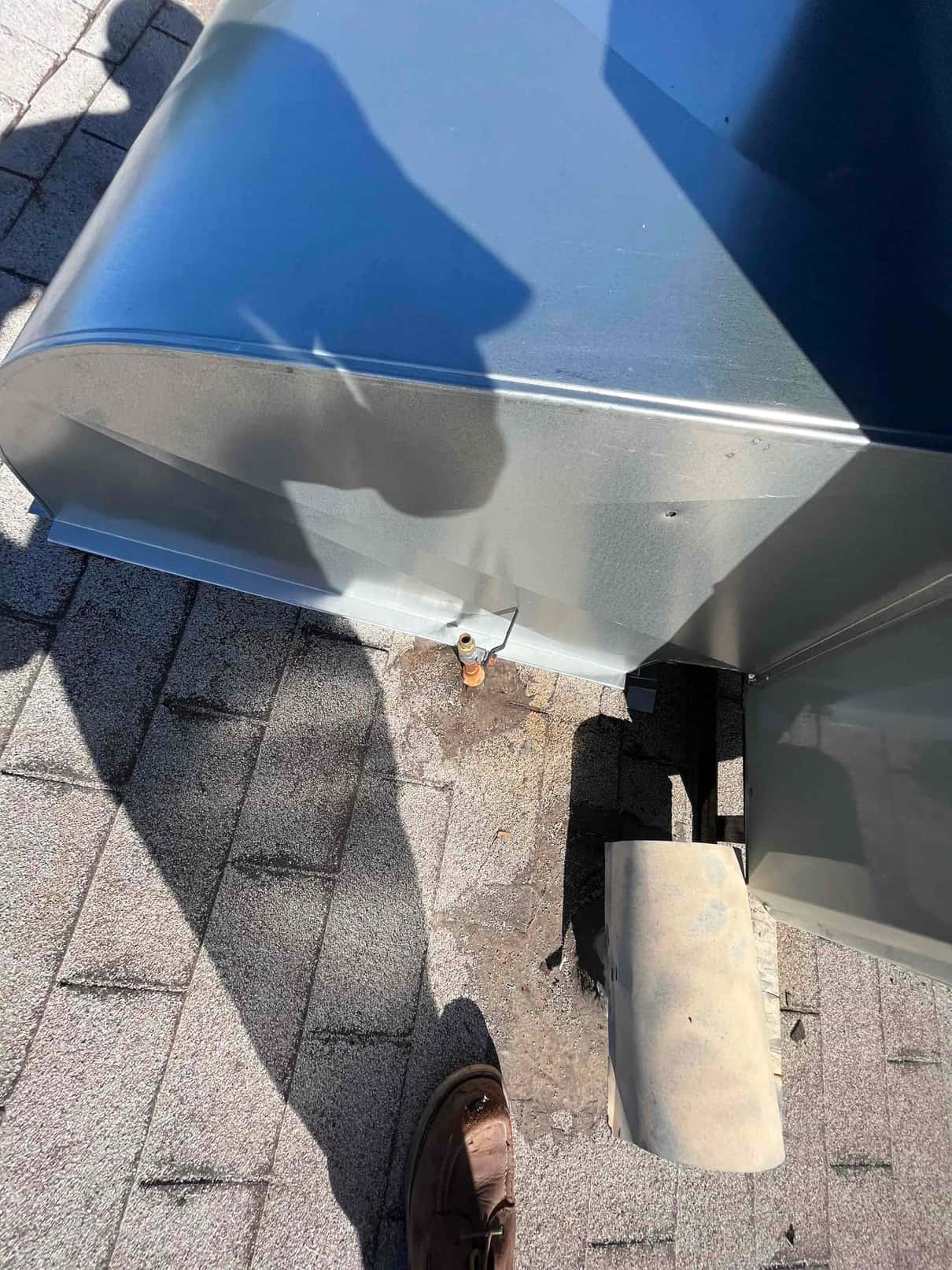 Rooftop curb and metal duct transition at a new HVAC unit, showing sealed penetration and roof shingles around the base.
