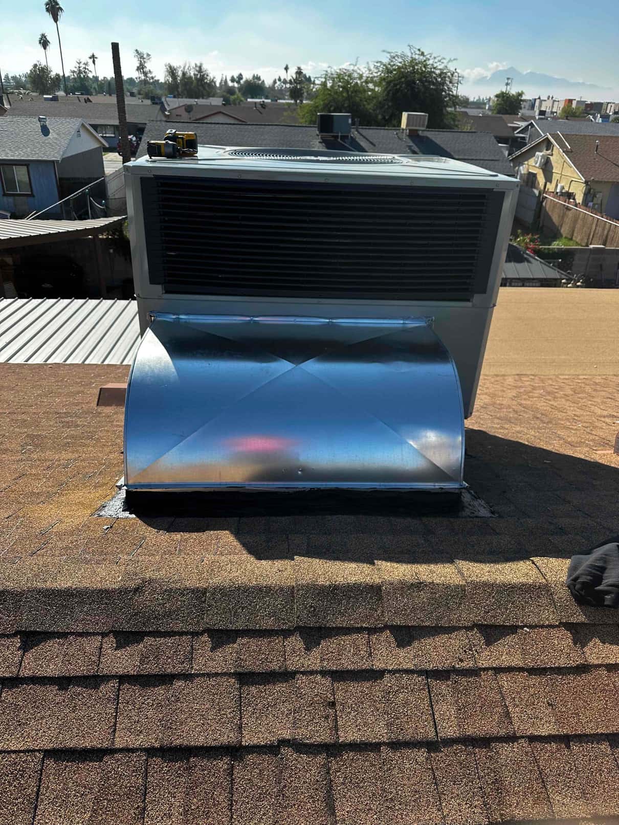 Rooftop package unit newly set on shingles with fabricated curb and sealed duct transition to the roof opening.