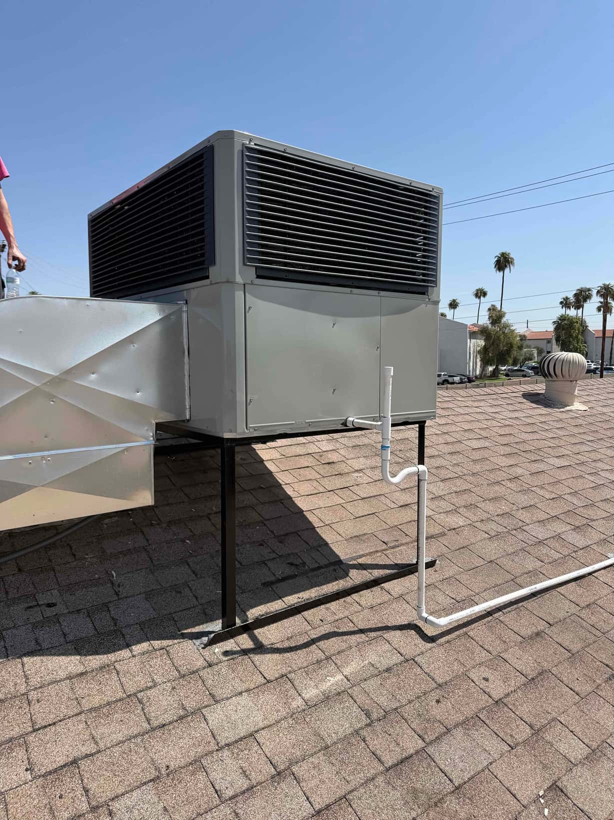 Rooftop packaged HVAC unit installed on a stand with connected duct transition and insulated condensate drain piping routed across the roof.