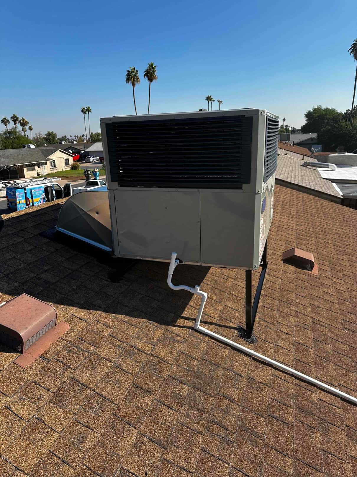Rooftop packaged HVAC unit installed on stand with secured condensate drain piping routed across the shingle roof.