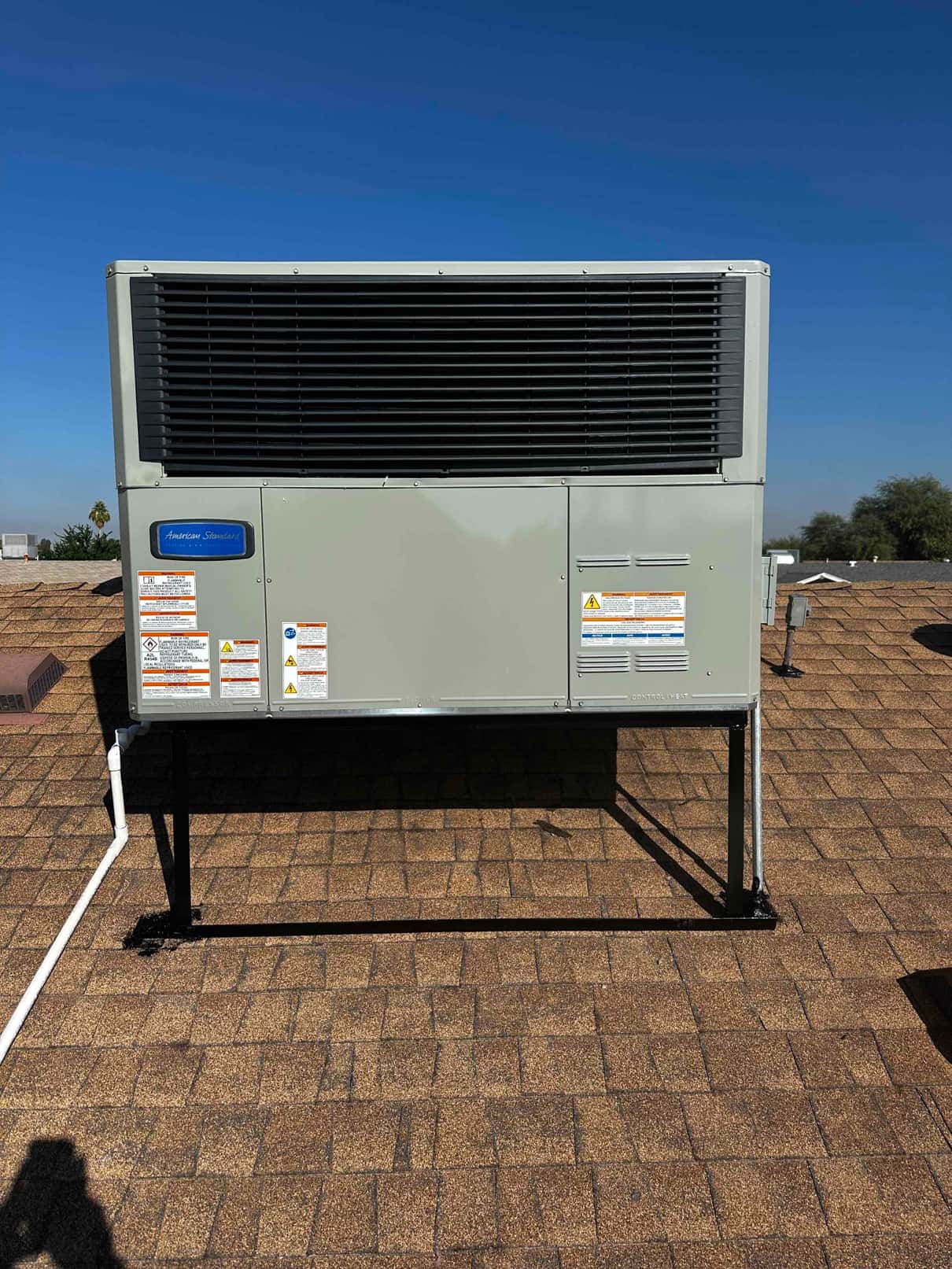 Rooftop packaged HVAC unit mounted on a metal stand with drain piping routed across the shingles after installation.