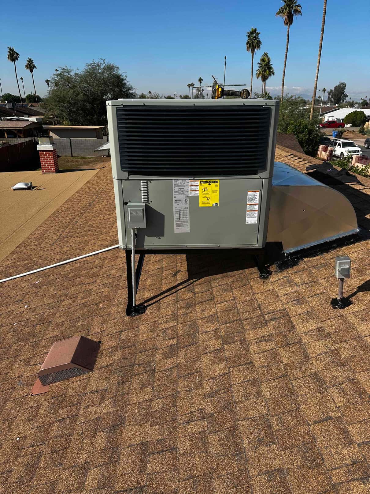 Rooftop packaged HVAC unit newly set on stands with sealed roof penetrations and adjacent duct transition, disconnect, and line set.