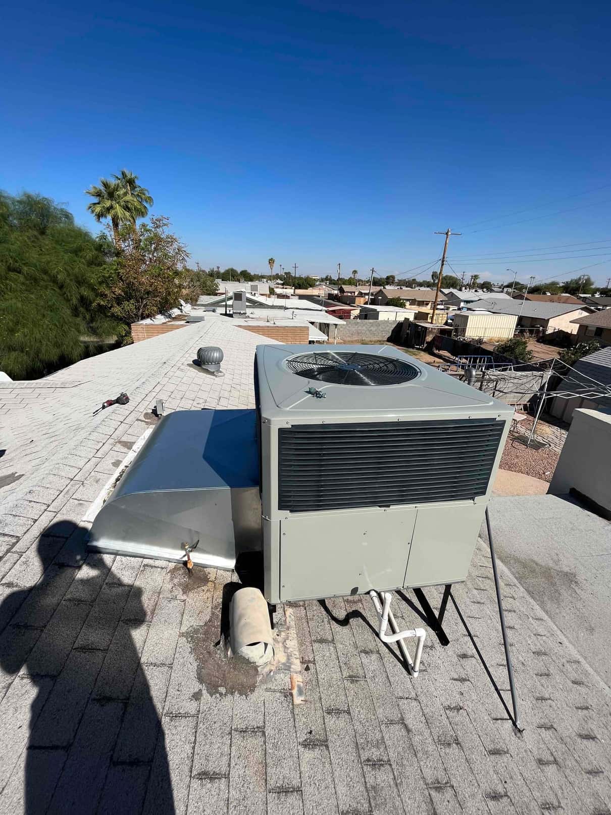 Rooftop packaged HVAC unit set on curb with connected duct transition and condensate drain piping, photographed during installation.