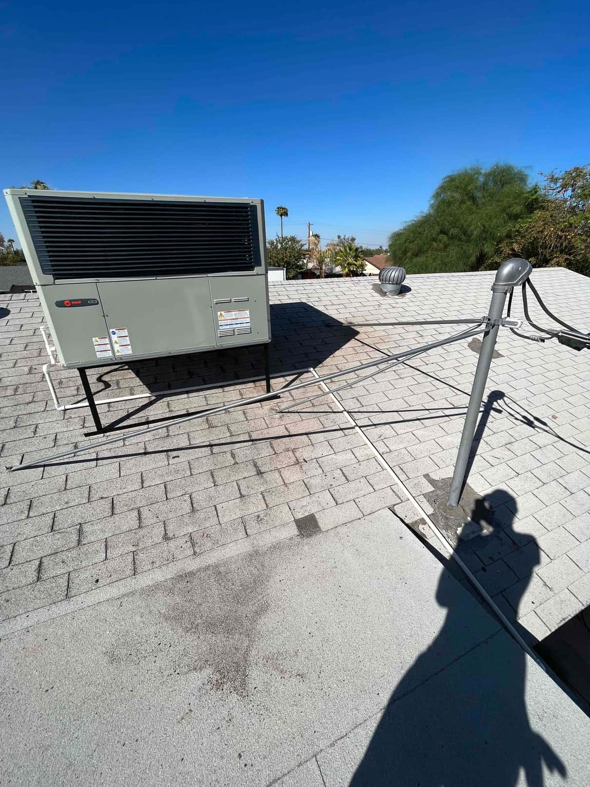 Rooftop packaged HVAC unit set on a raised stand with new electrical conduit routed across the shingle roof.