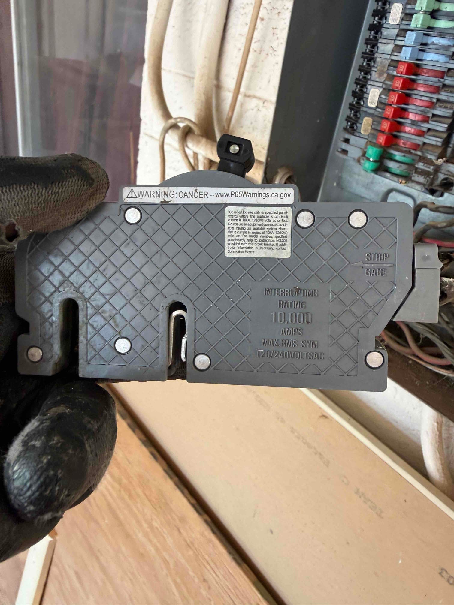 Technician holds a circuit breaker near the electrical panel during HVAC install, showing interrupting rating and wiring gauge reference.