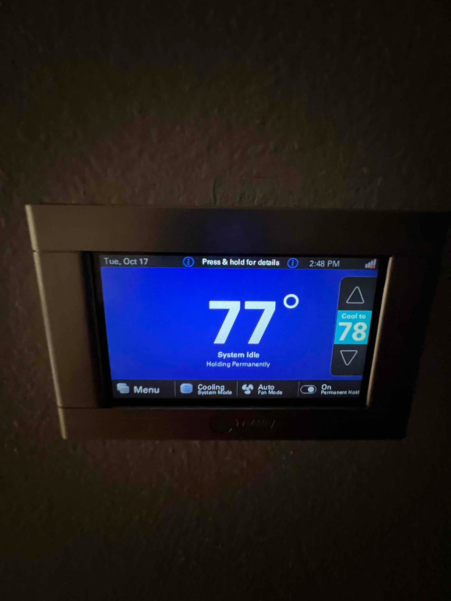 Wall-mounted touchscreen thermostat displays 77 degrees with system idle, cooling mode selected, and fan set to auto.